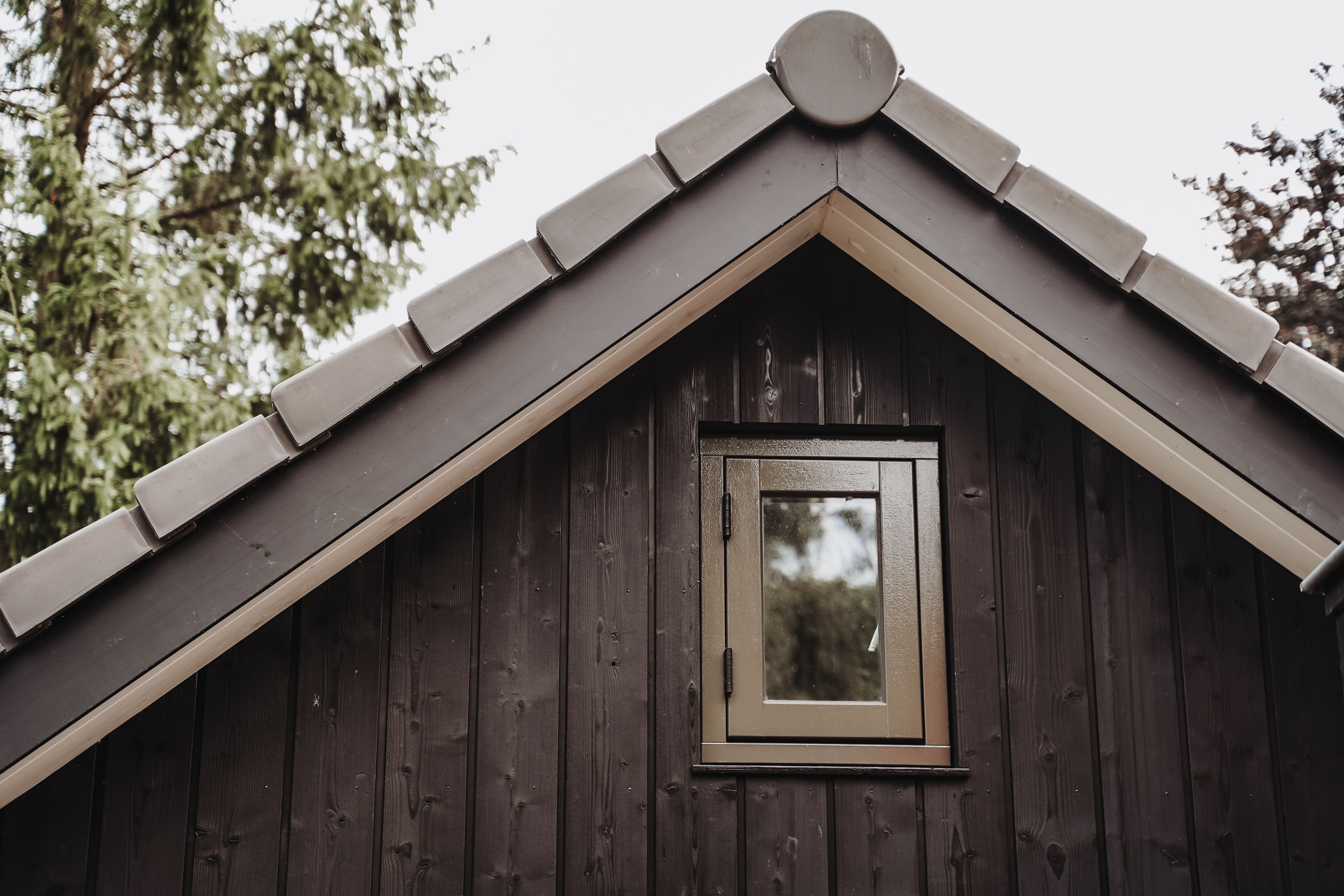 Dak van een houten huis met een klein vierkant raam en grijze dakpannen
