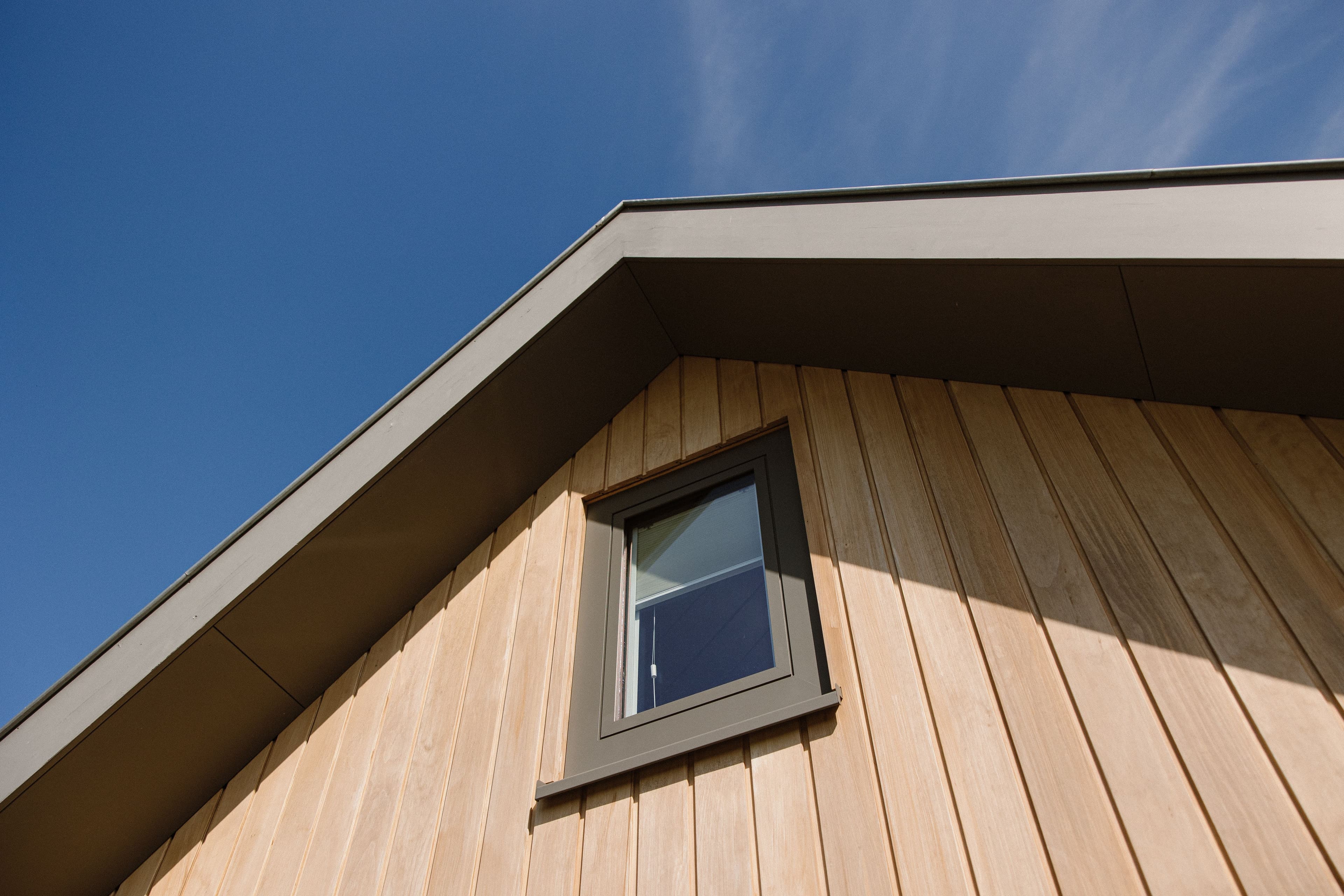 Dakrand en gevel van een houten huis met klein rechthoekig raampje en blauwe lucht
