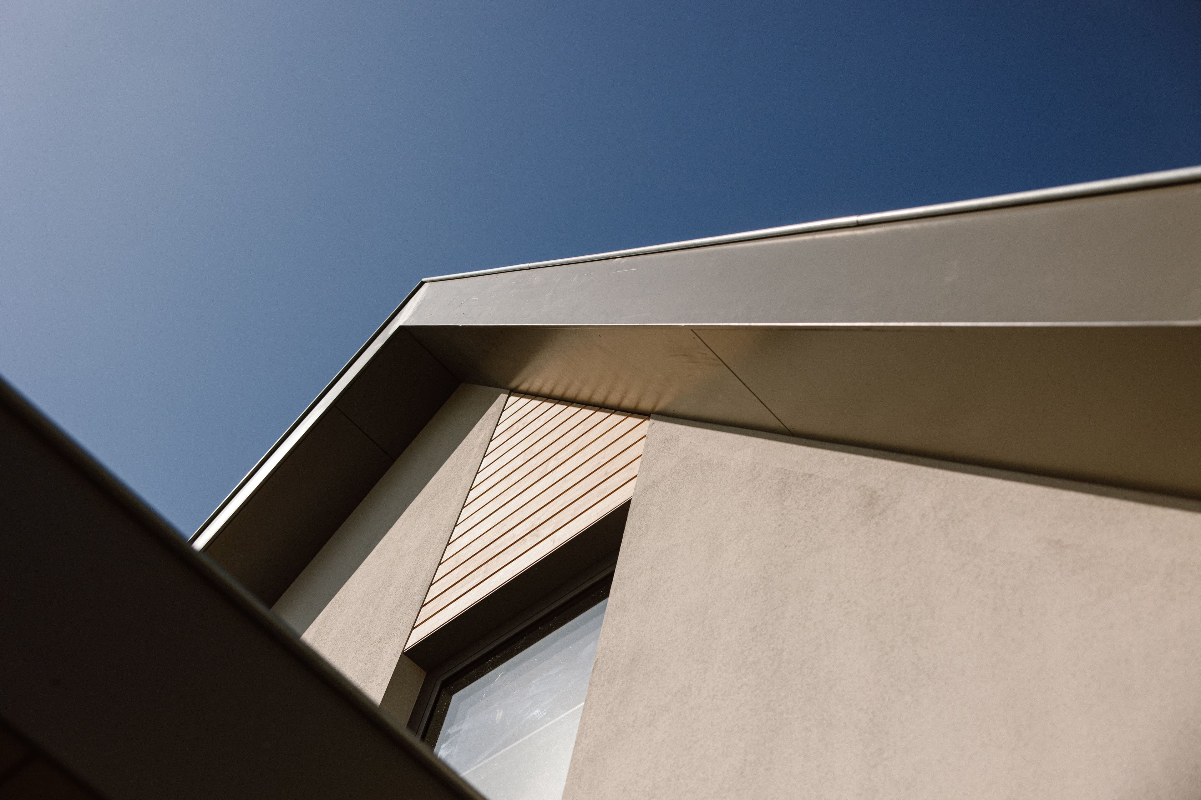Detail van een moderne gevel met overstekend dak, houten lamellen en raam tegen een blauwe lucht