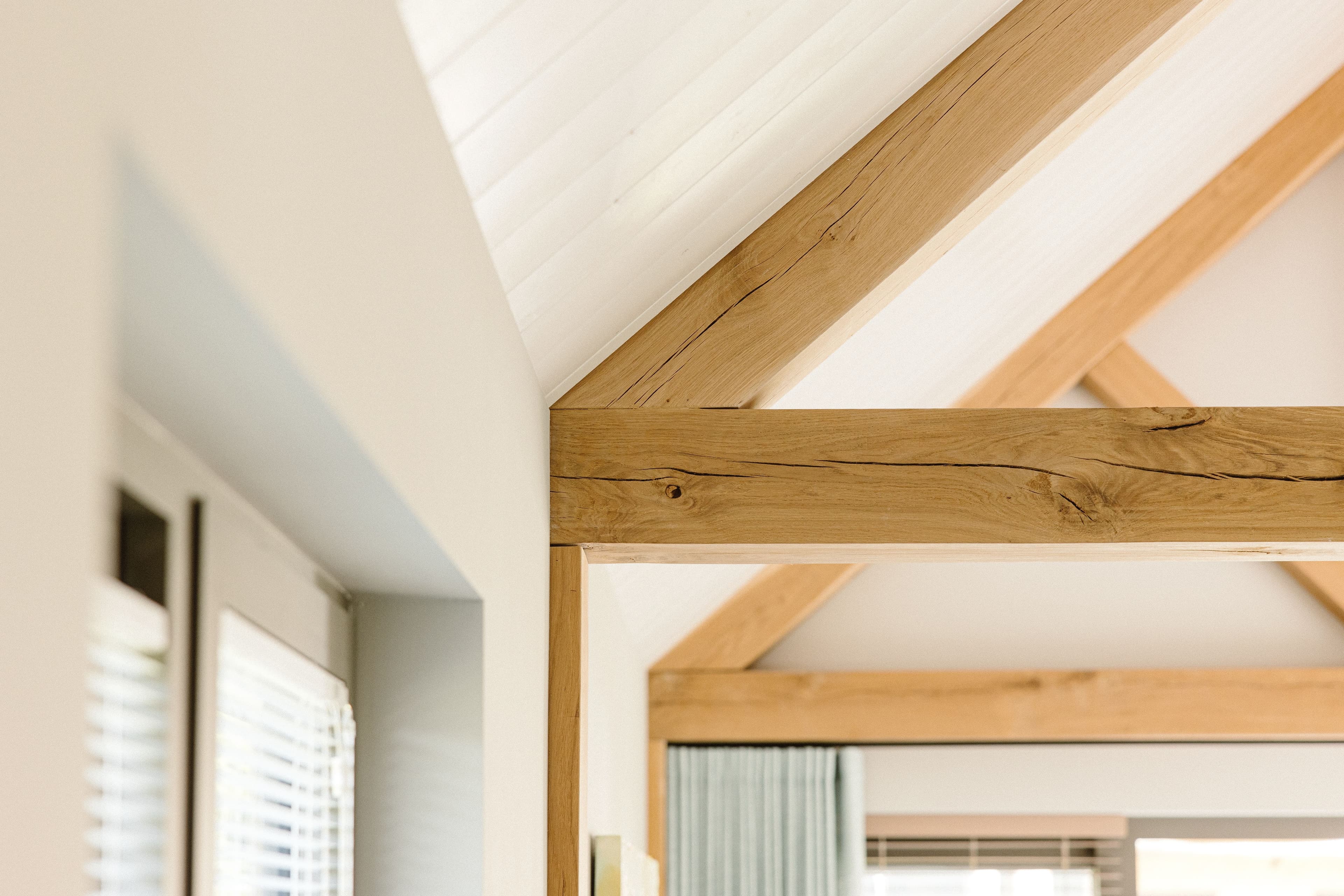 Houten balken en lichtkoepel in een modern interieur met witte muren en groene gordijnen