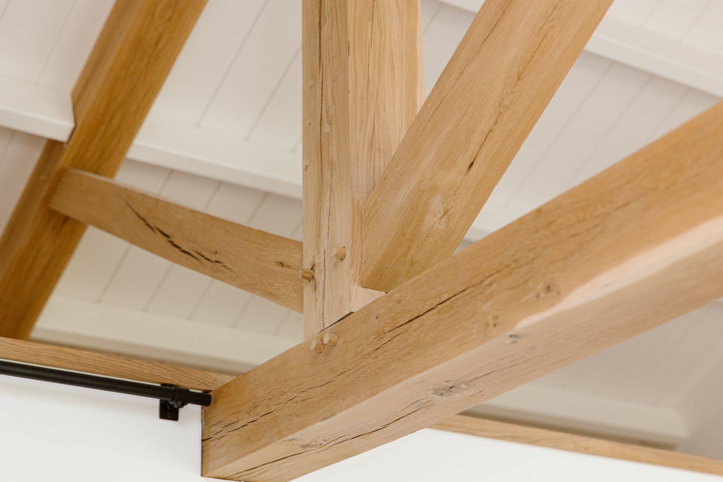 Close-up van houten balken aan het plafond met een metalen gordijnroede eronder