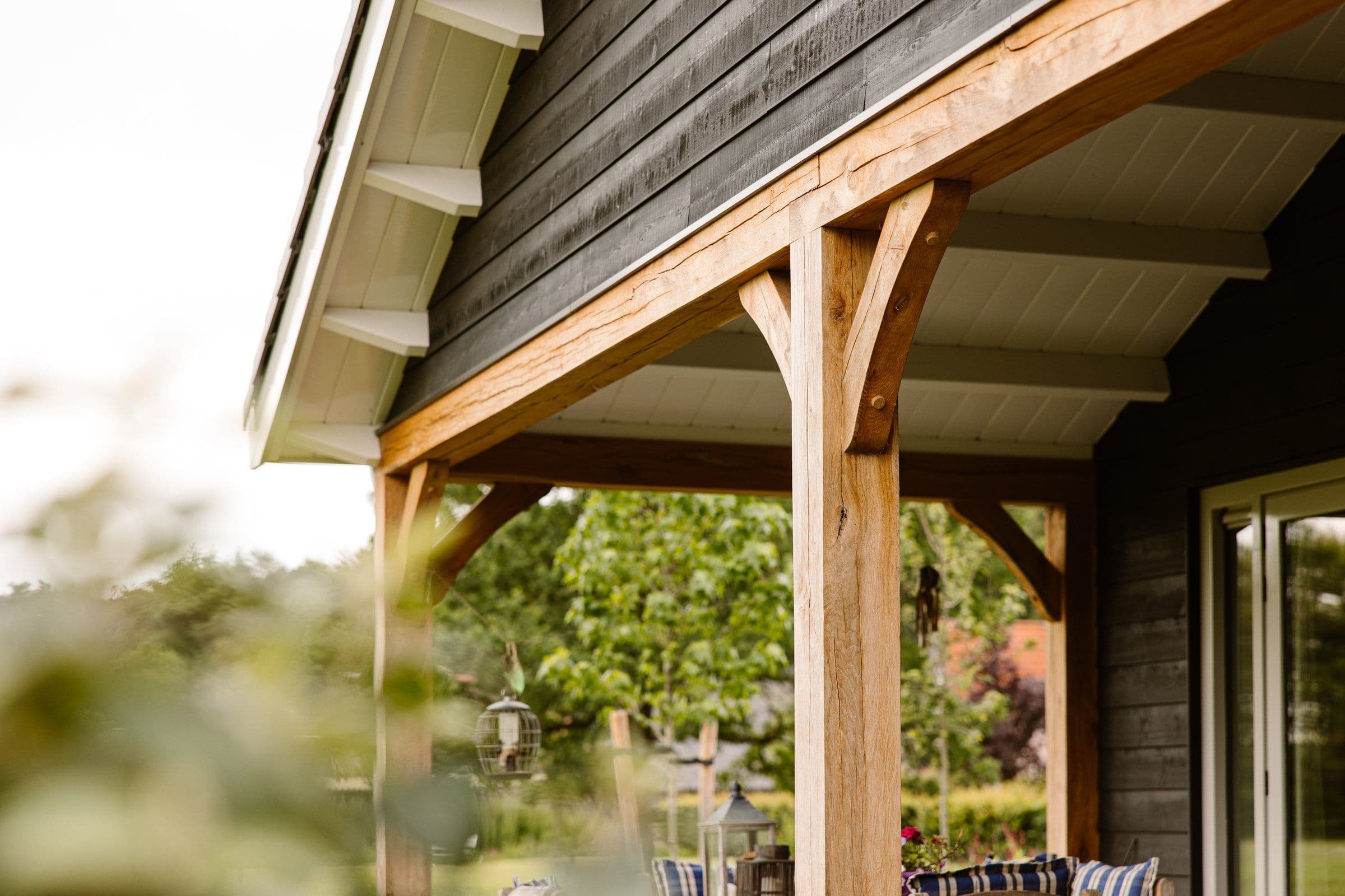 Houten veranda met stevige balken en witte overkapping aan huiszijde met groene tuin op achtergrond