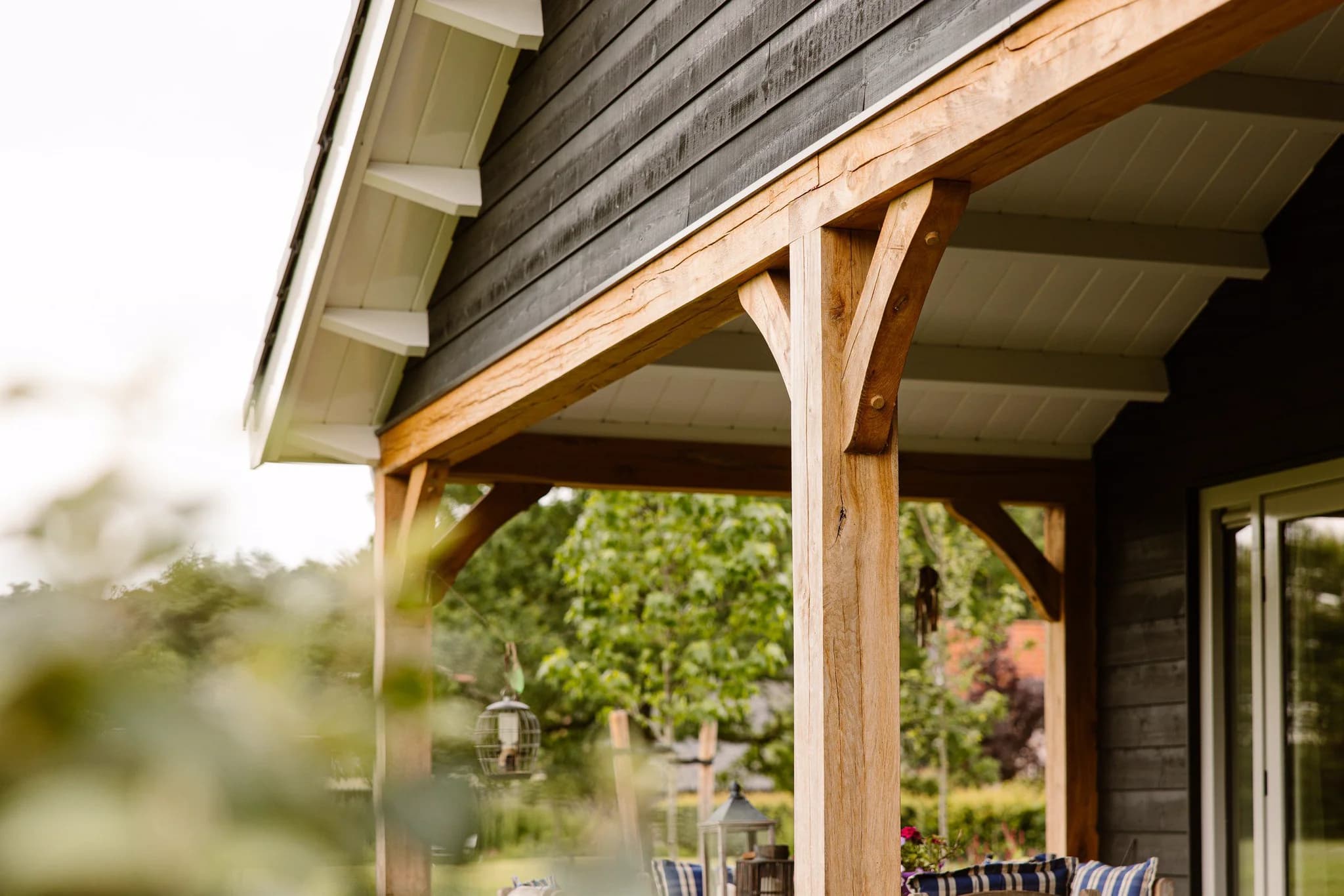 Houten veranda met stevige balken en witte overkapping aan huiszijde met groene tuin op achtergrond
