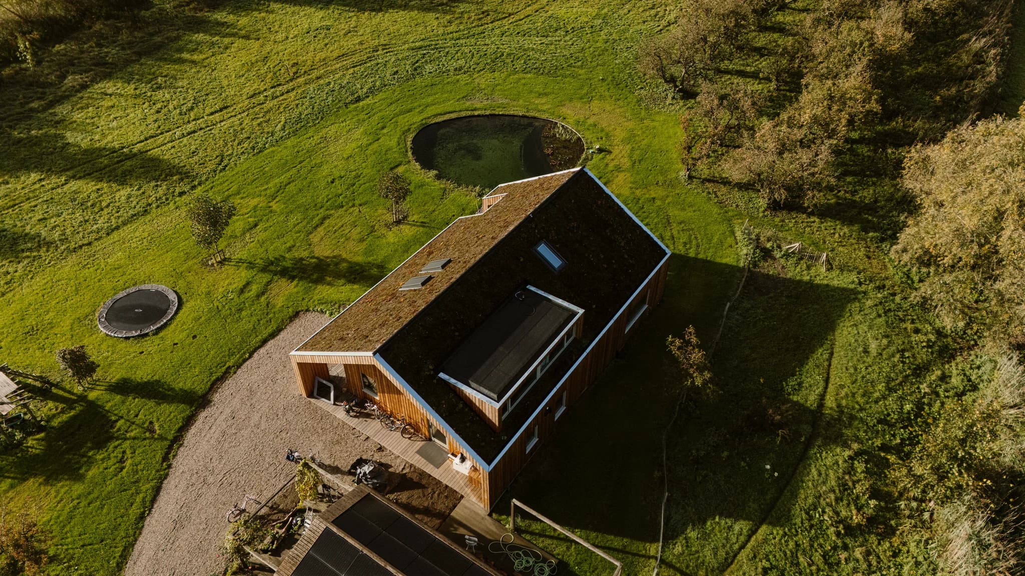 Luchtfoto van een huis met groen begroeid dak en vijver in tuin omgeven door gras en bomen