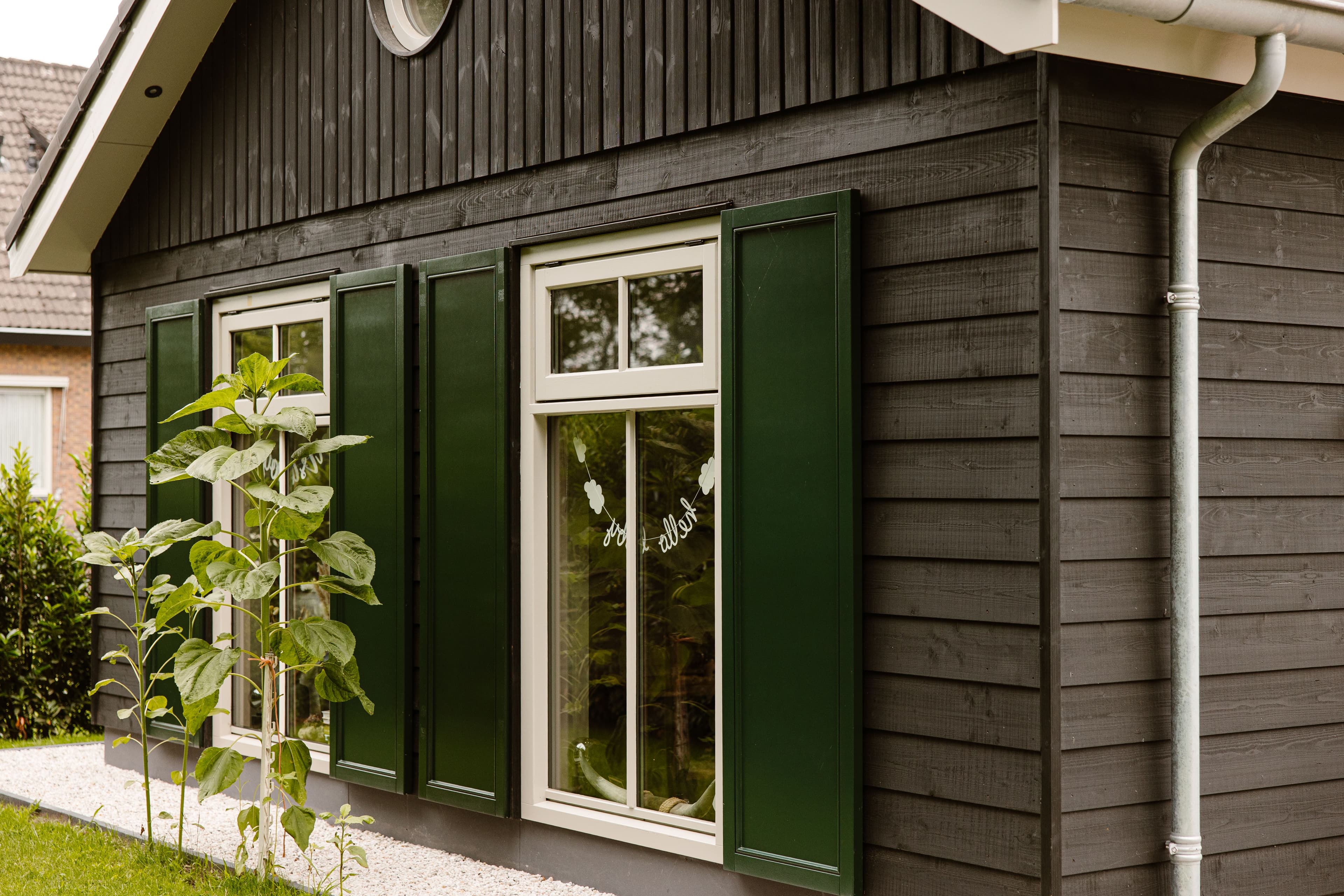 Zijaanzicht van een houten huis met groene luiken en witte ramen