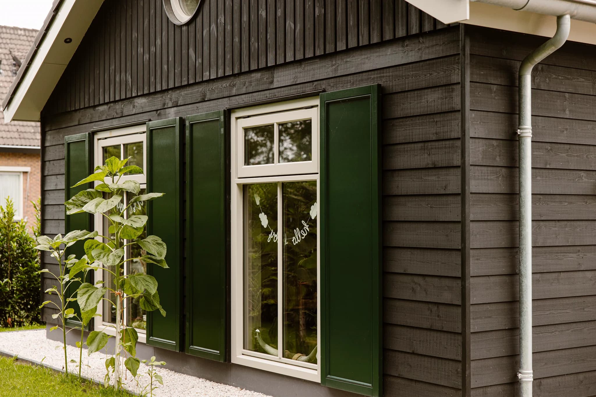 Zijaanzicht van een houten huis met groene luiken en witte ramen