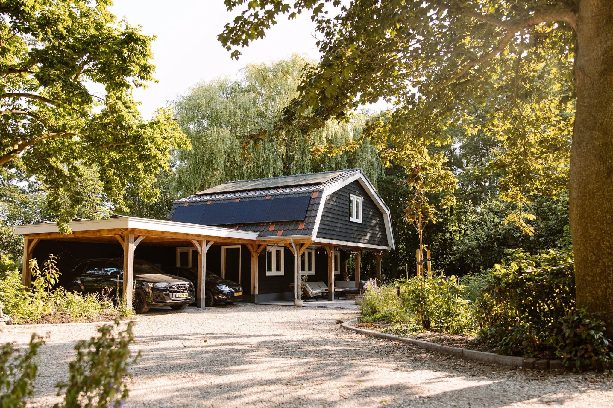 Donker houten huis met zonnepanelen op het dak, overkapping met twee auto's en een groene tuin