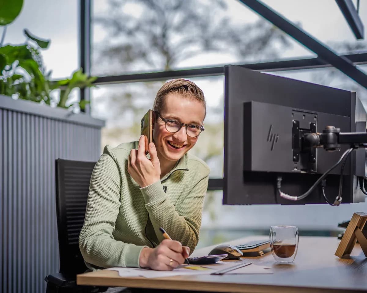 Jonge man met bril die aan een bureau werkt en telefoneert met een gouden mobiele telefoon op kantoor.