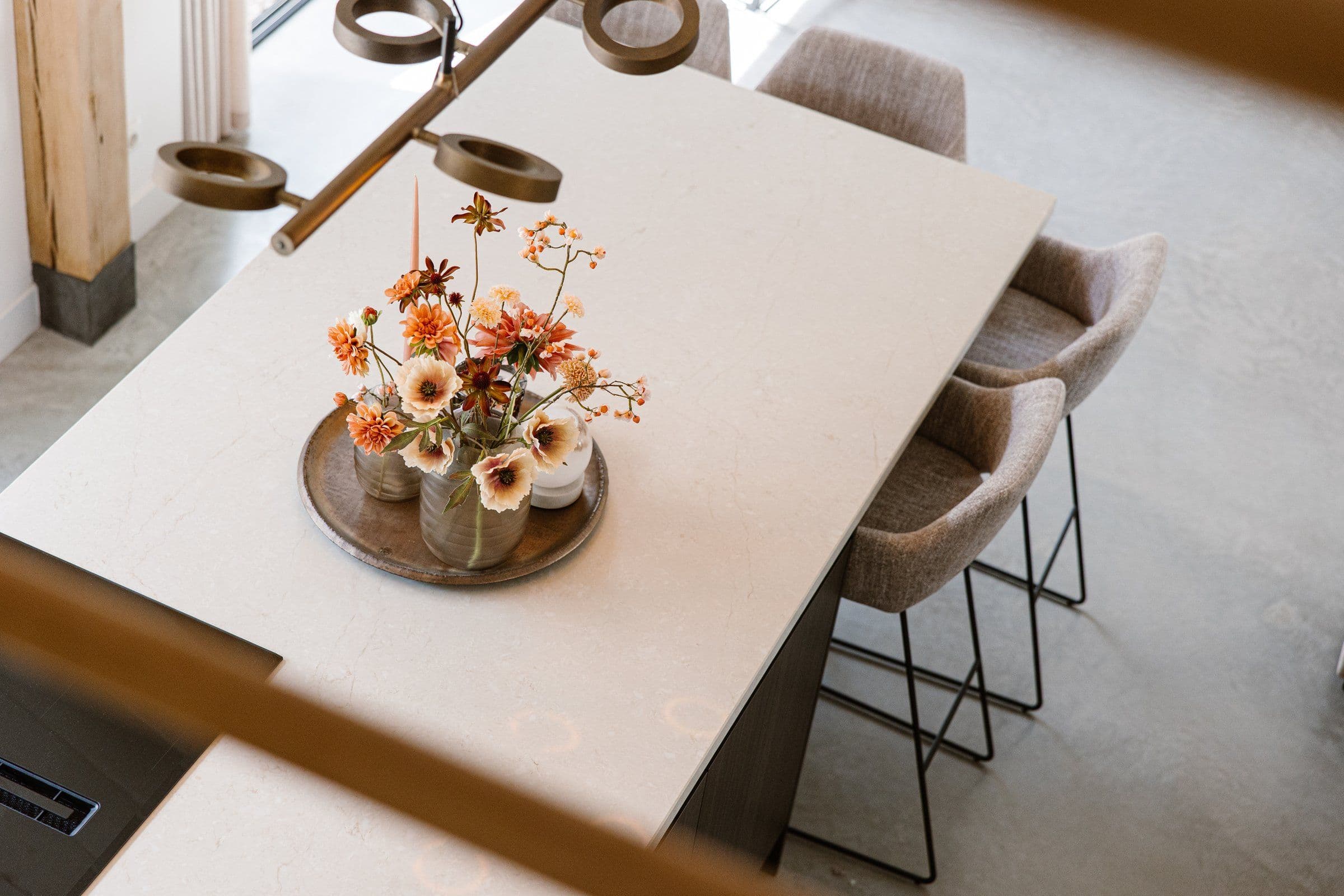 Witte marmeren keukentafel met oranje bloemen op een houten serveerschaal en drie stoffen barkrukken