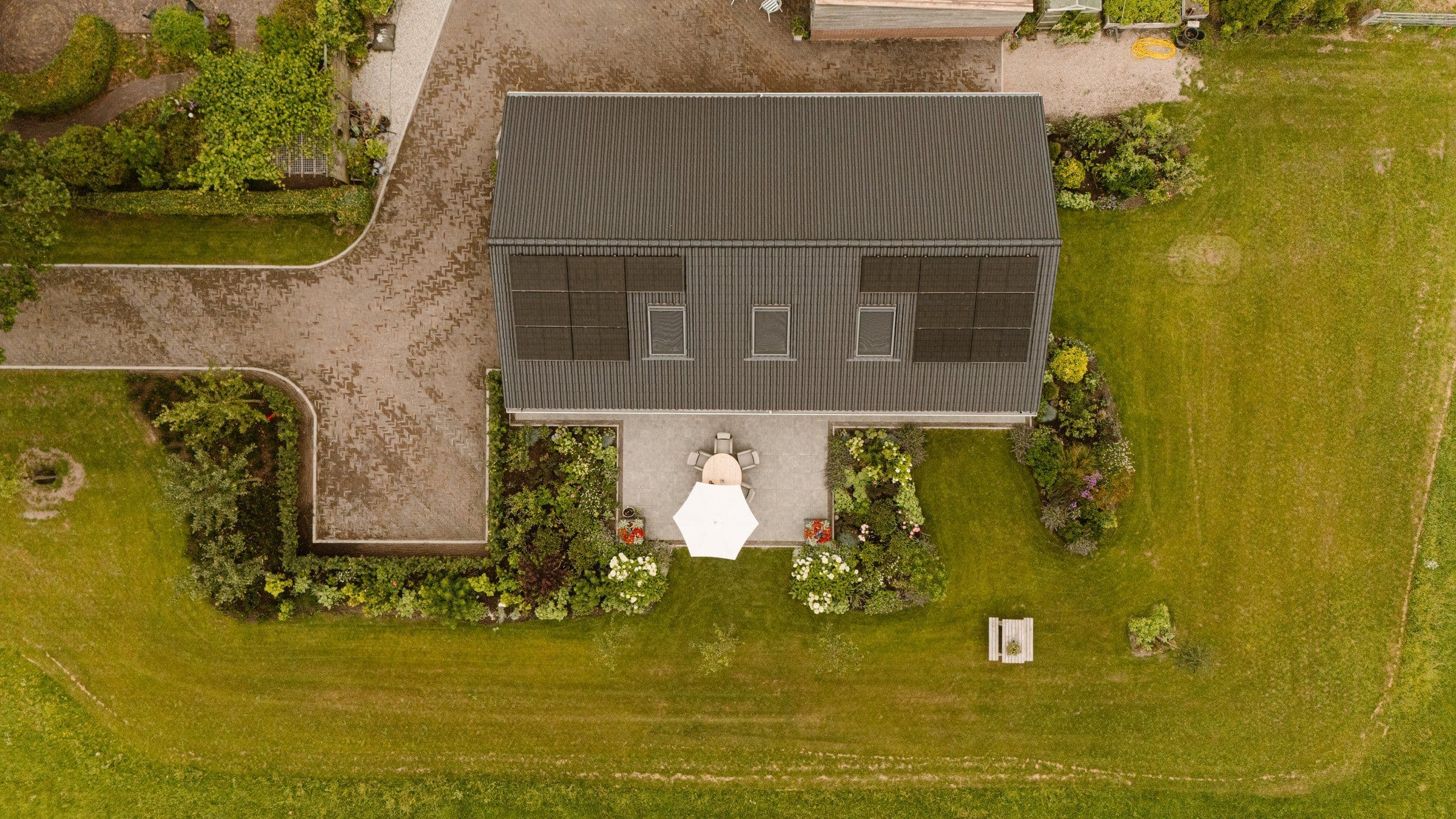 Luchtfoto van een huis met een grijs dak met zonnepanelen en een tuin met terras en gras