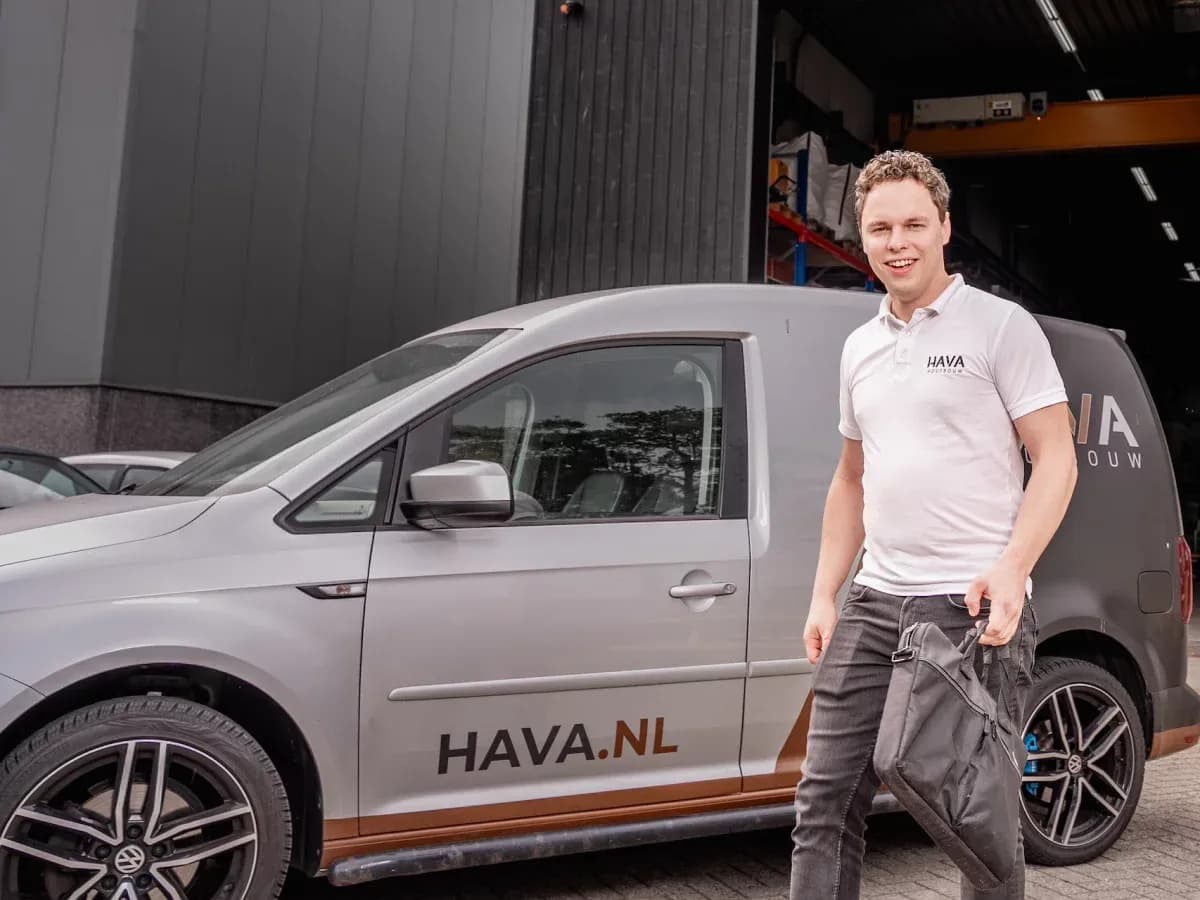 Man met wit poloshirt naast grijze bestelauto met HAVA.NL tekst bij bedrijfspand