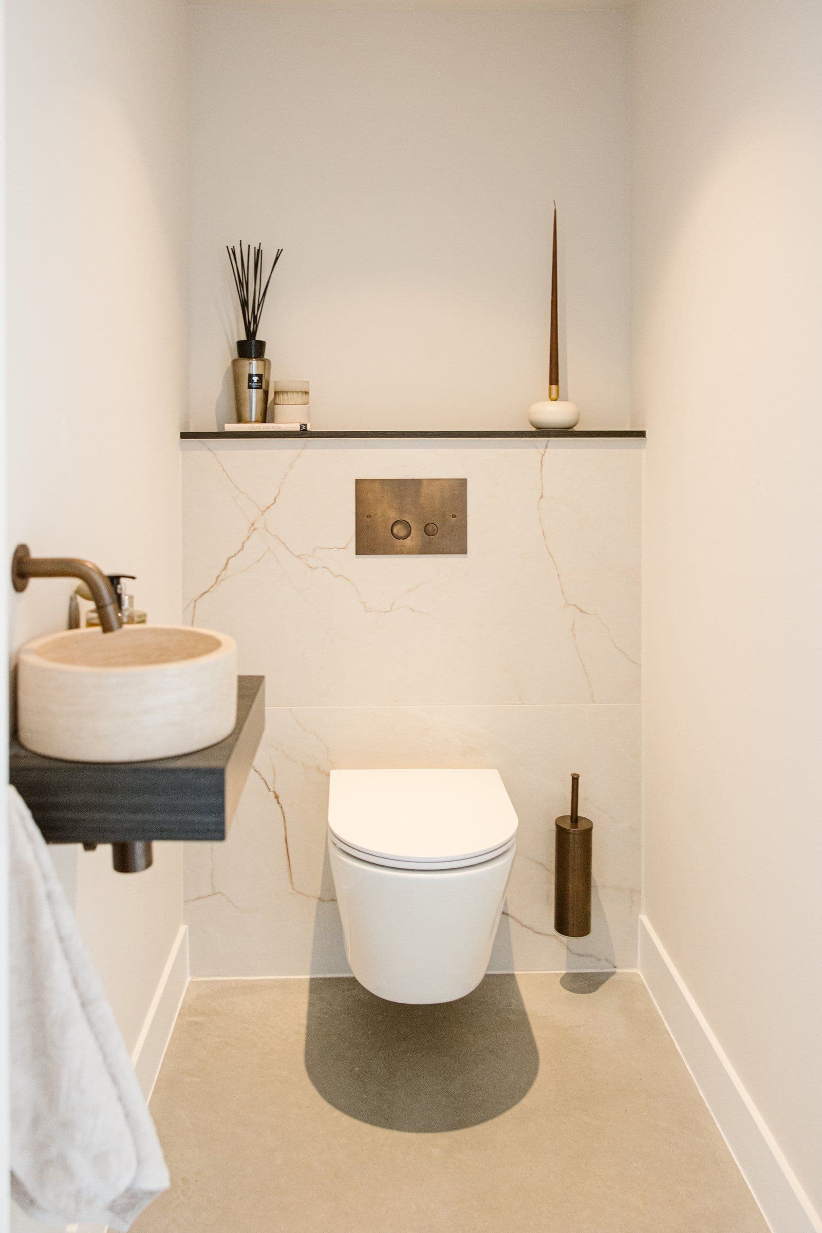 Minimalistisch licht toilet met wit wandcloset, marmeren achterwand, houten waskom en decoratieve objecten op een plank