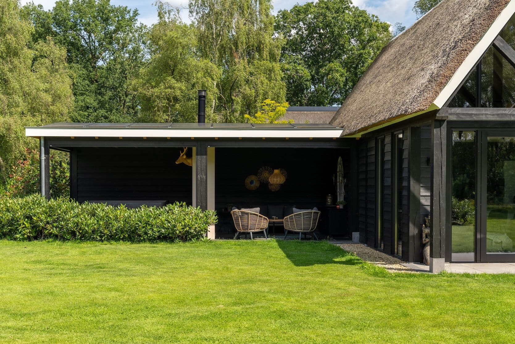 Modern landelijk huis met rieten dak en een overdekt terras met rotan stoelen in een groene tuin