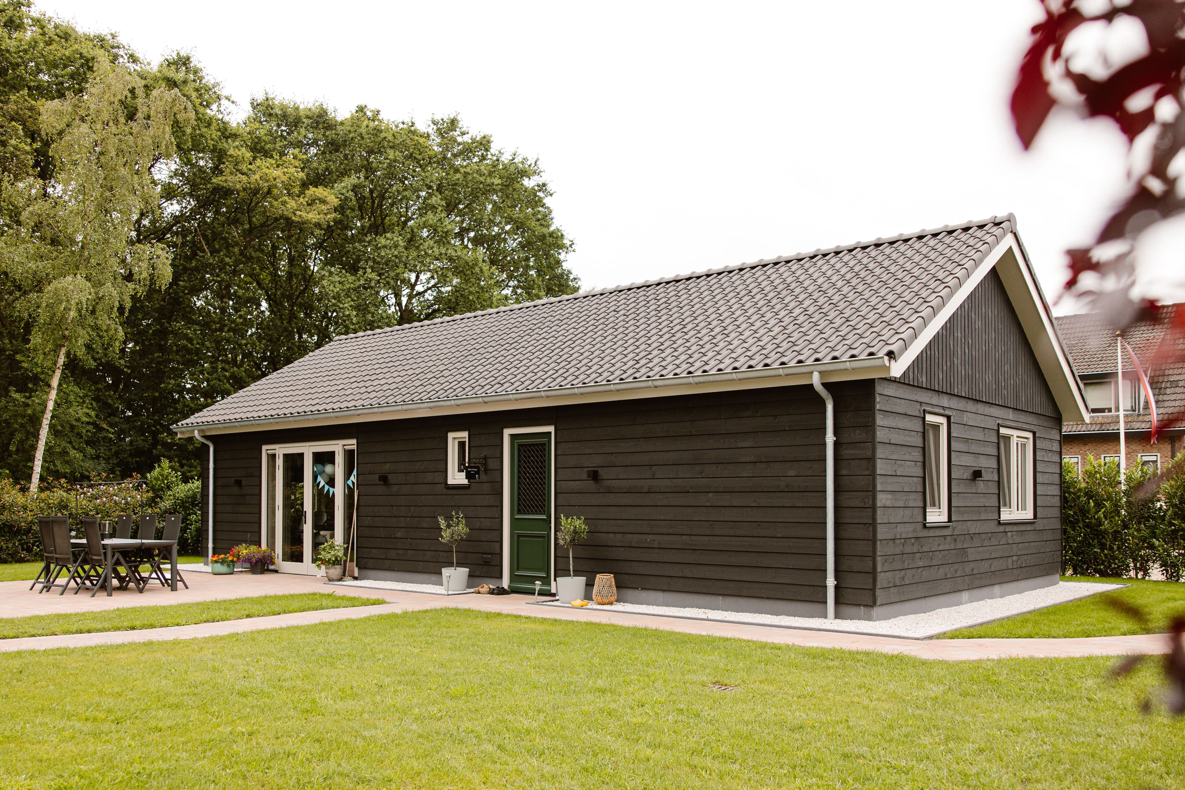 Moderne bungalow met zwarte gevel en grijs pannendak in een groene tuin