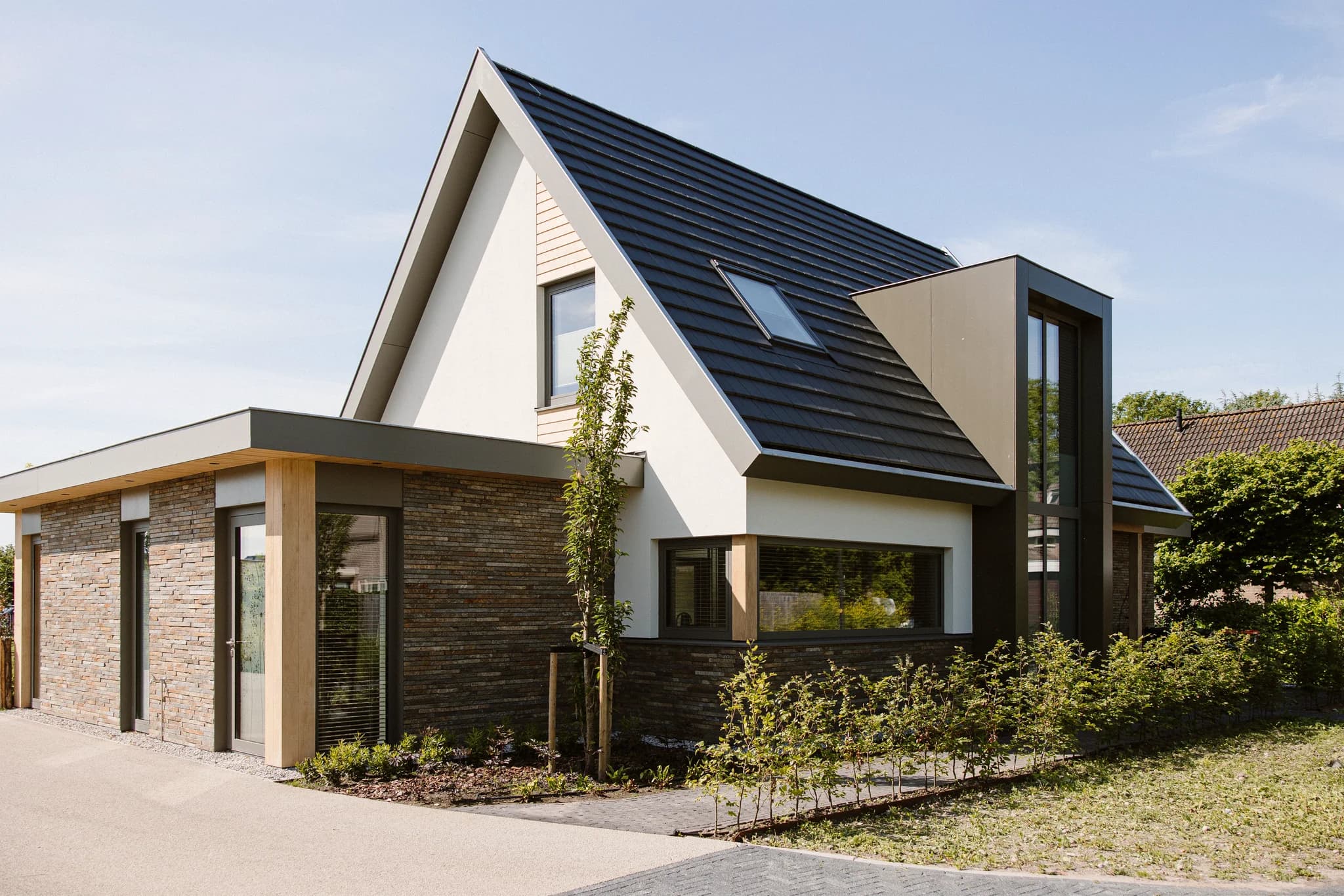 Moderne eengezinswoning met bakstenen gevel, wit stucwerk, schuin dak met dakraam en kleine tuin met jonge bomen en struiken