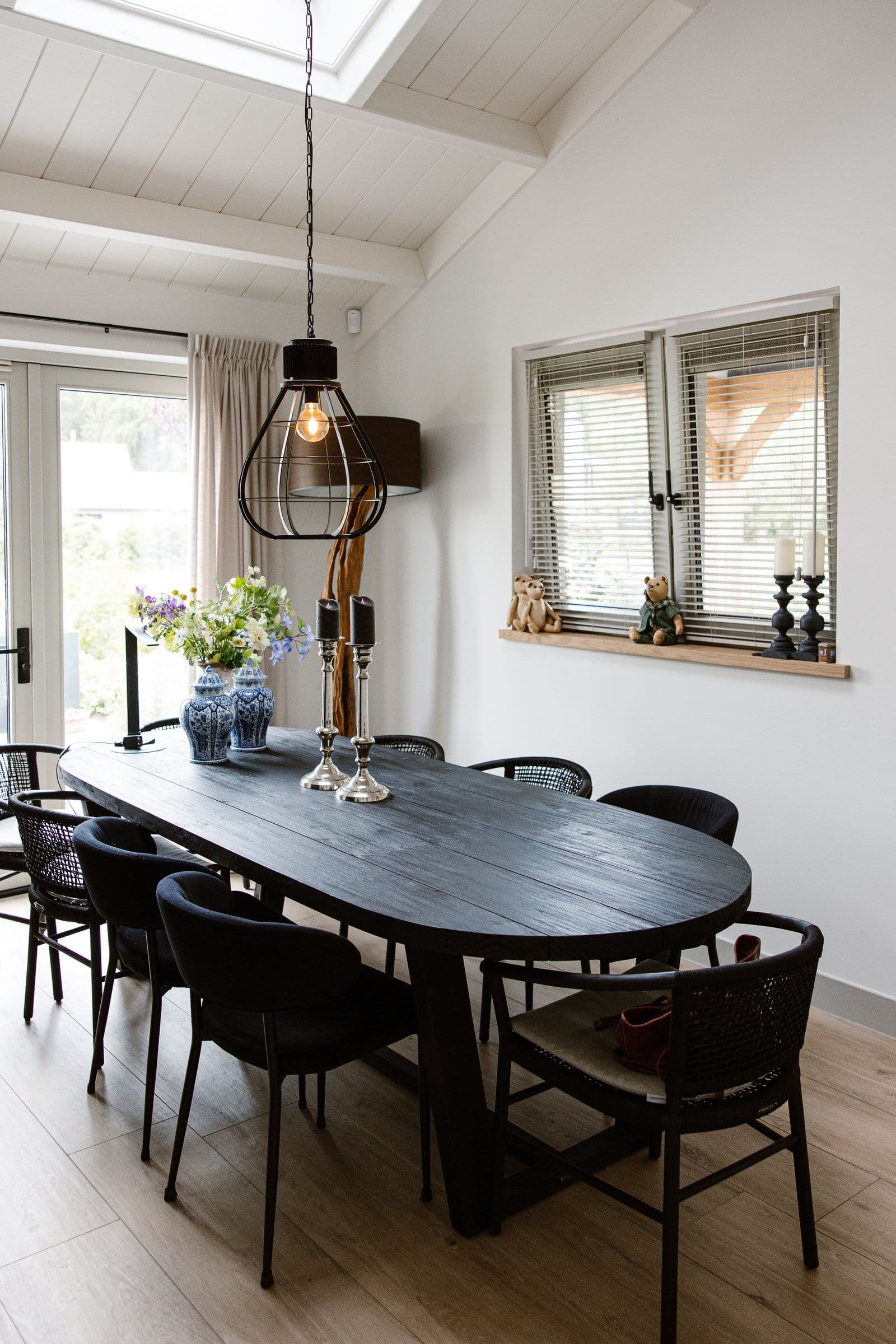 Moderne eetkamer met ovale donkere houten tafel, zes stoelen, hanglamp en raam met jaloezieën