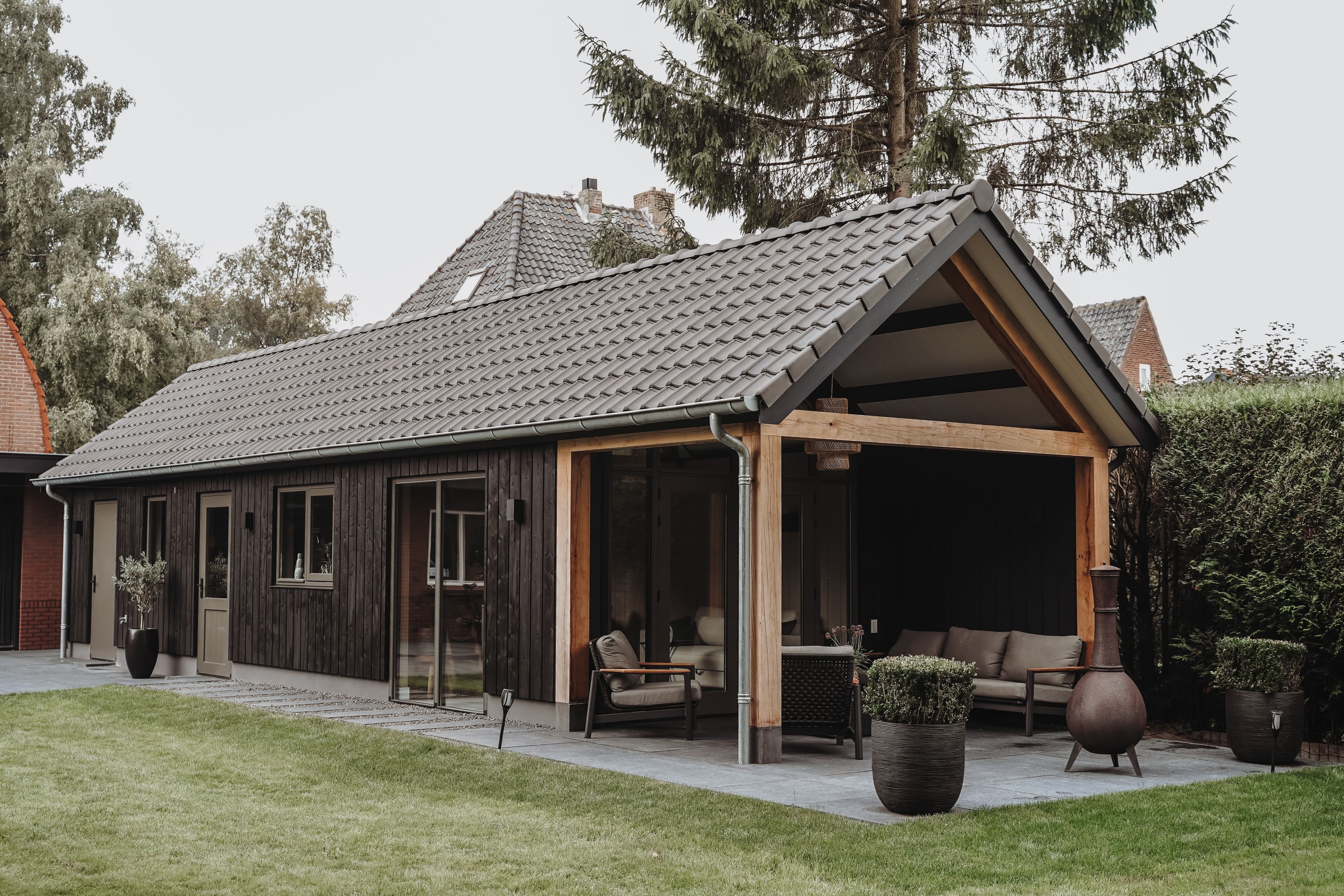 Buitenruimte met houten planken, overkapping, stoelen, plantenpotten en groen gazon