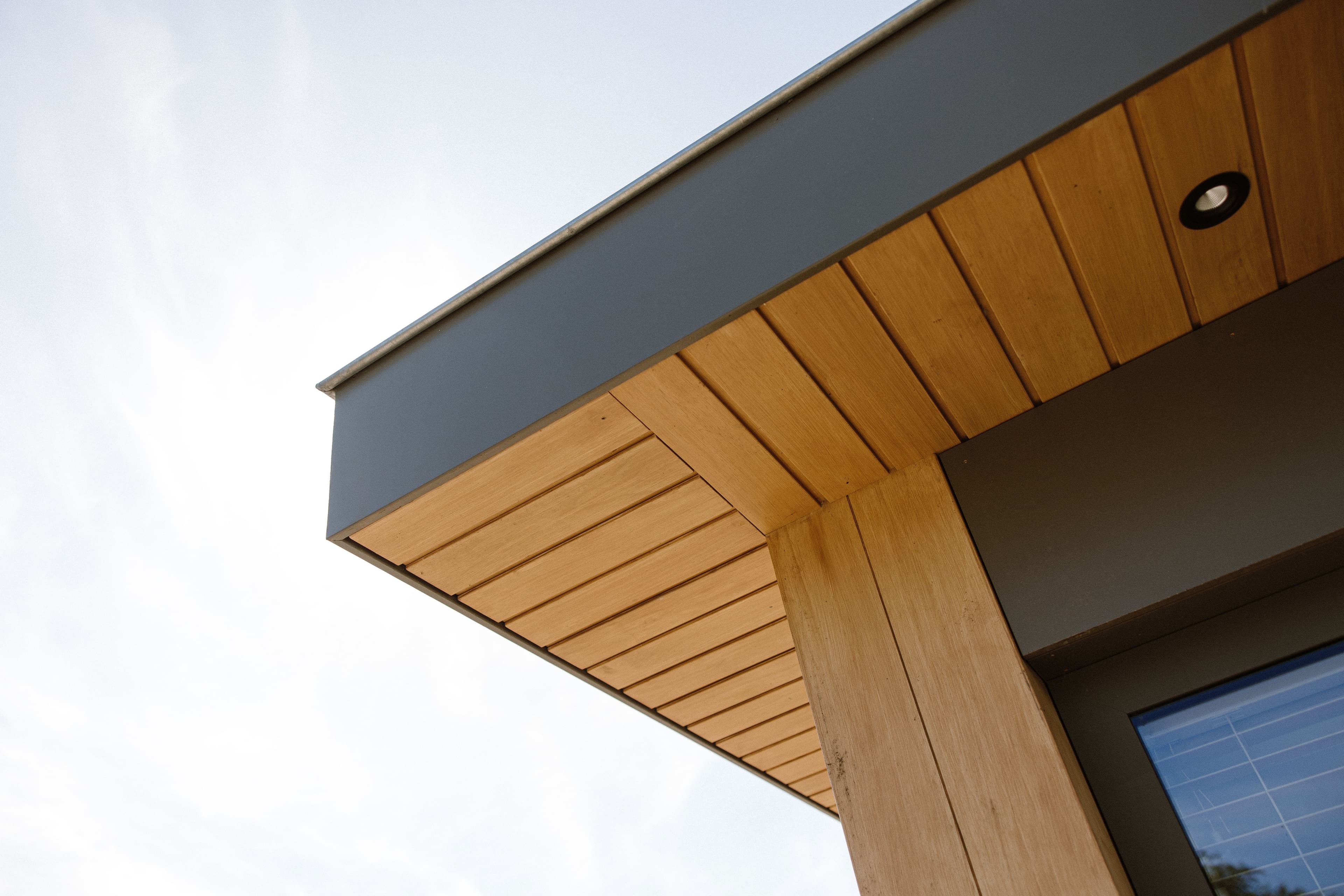 Hoek van een modern huis met houten gevelbekleding en een inbouwspot onder het dak overstek