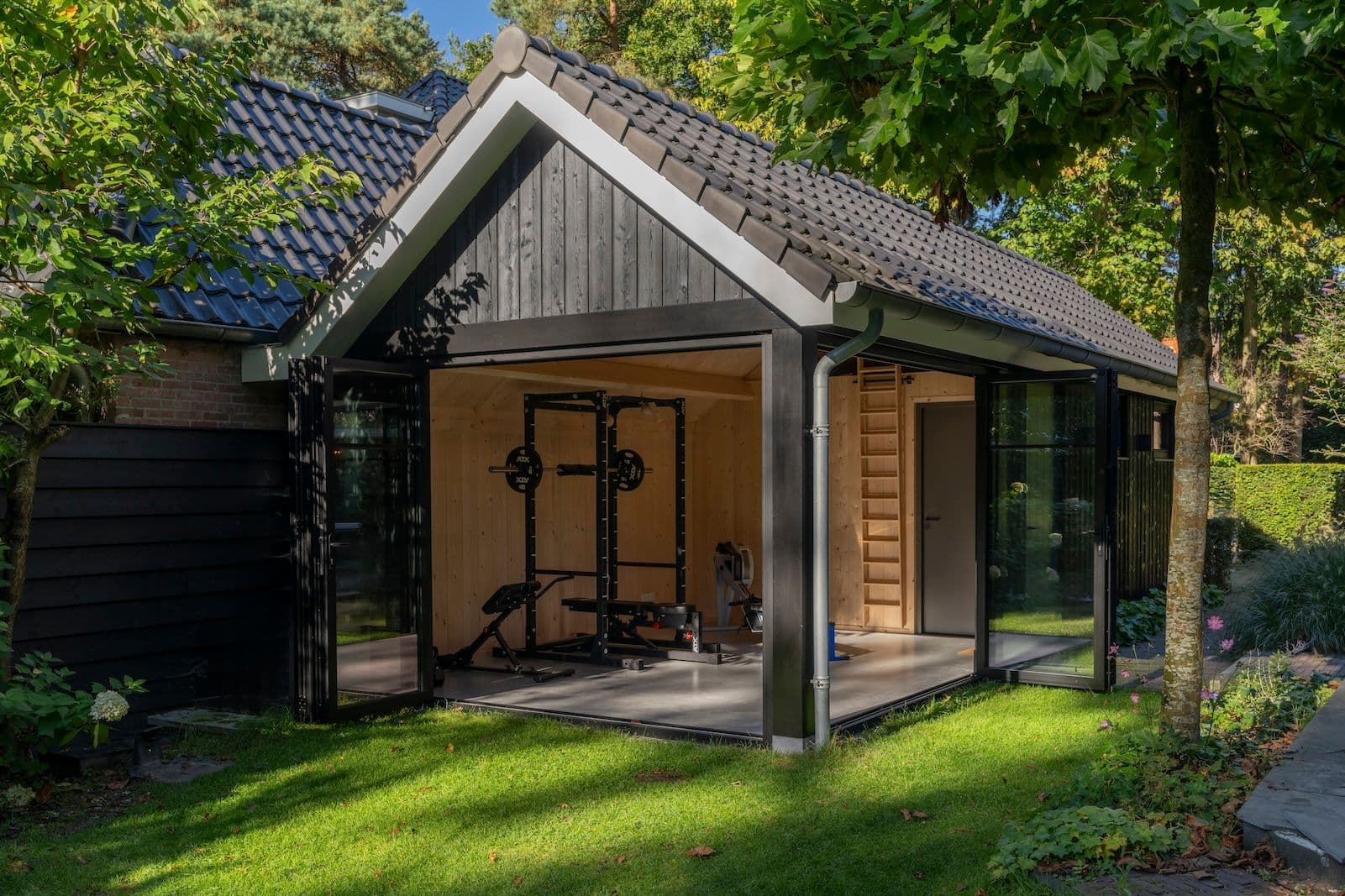 Houten tuinschuur met open vouwdeuren en fitnessapparatuur binnenin