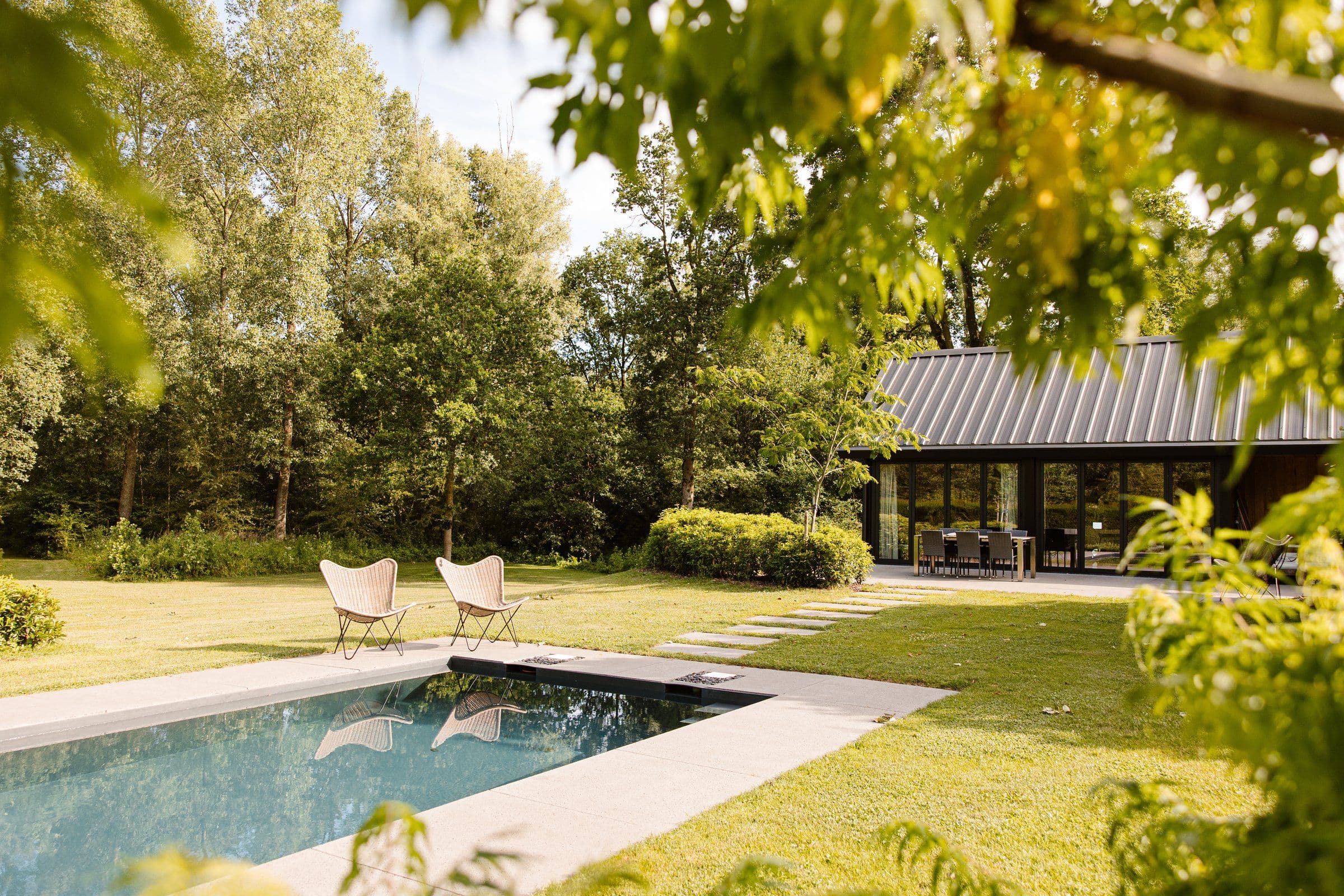 Tuin met zwembad, twee rieten stoelen en een modern huis met glazen schuifdeuren