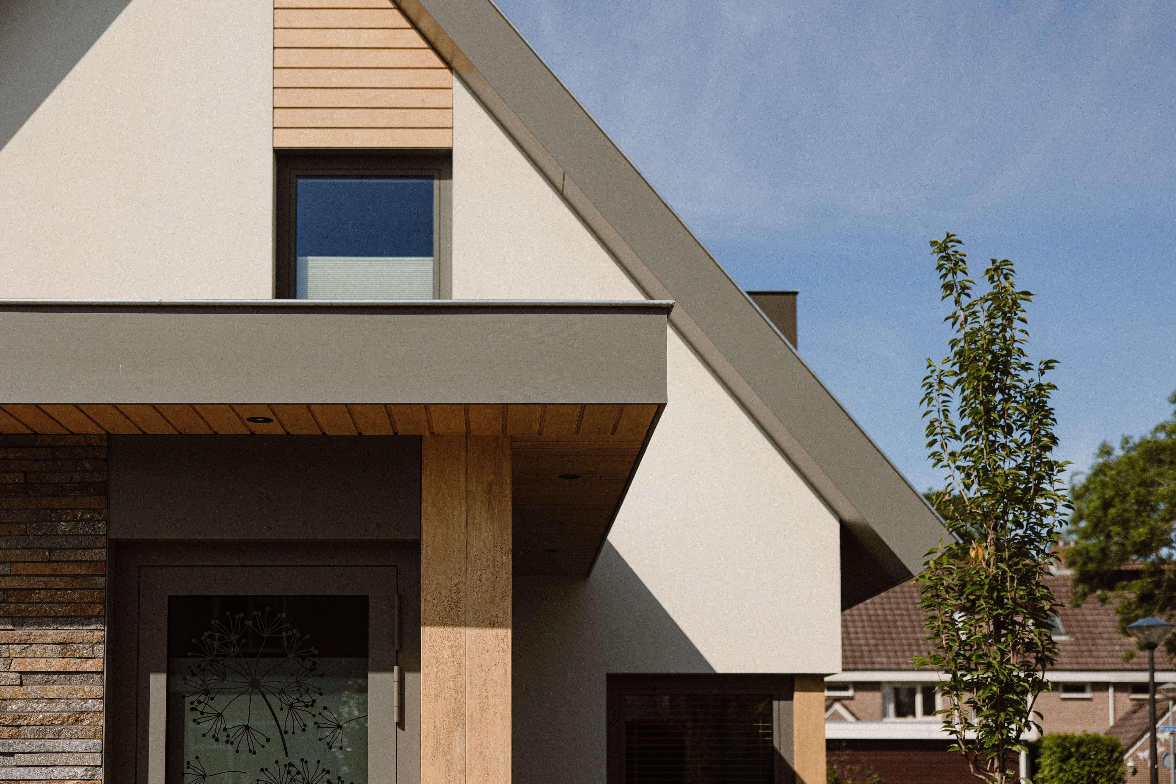 Moderne woning met schuine daklijn, houten accenten en decoratieve glazen deur.