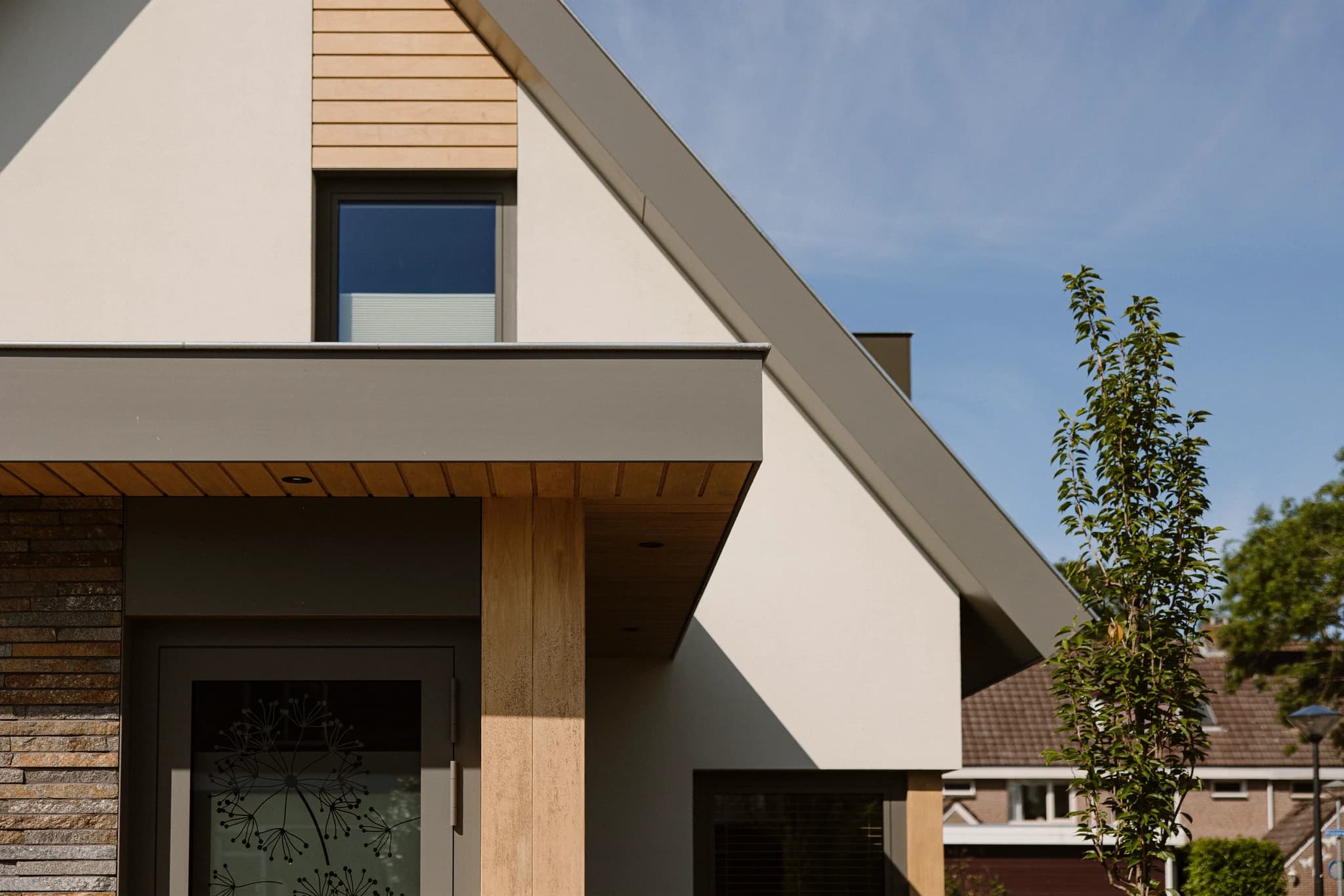 Moderne woning met schuine daklijn, houten accenten en decoratieve glazen deur.