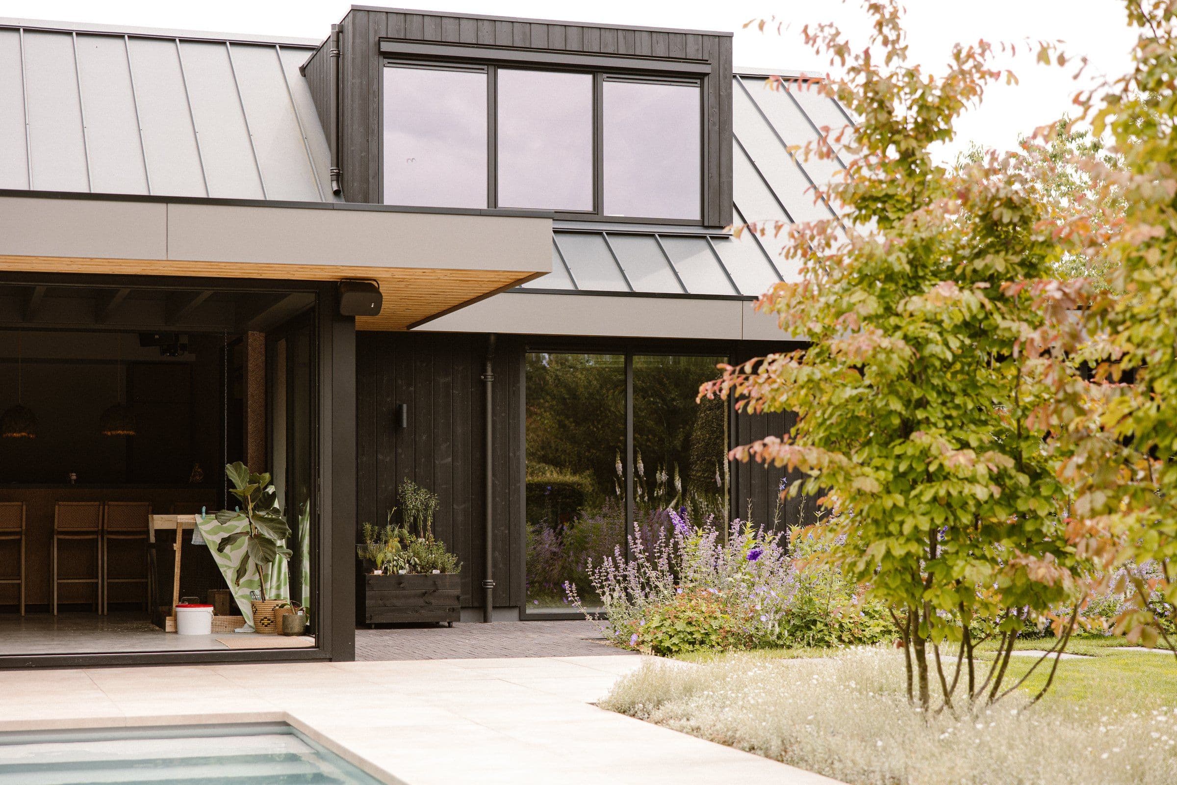 Moderne woning met open schuifdeur, tuin met bloemen en zwembad in de voorgrond