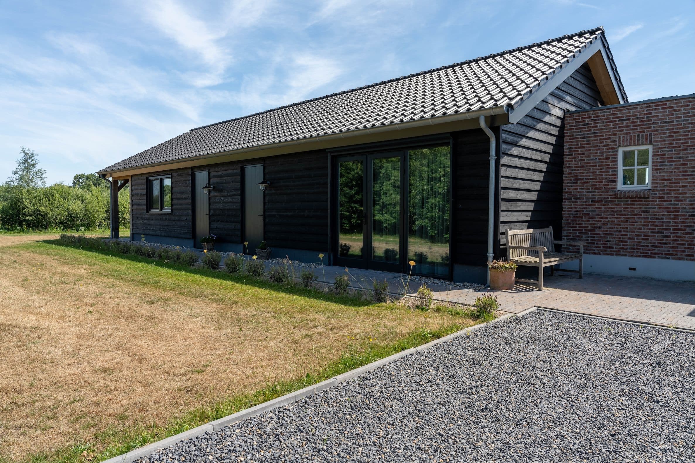 Woning met zwarte houten gevel en grijs pannendak, tuin met gras en planten, en een stenen pad