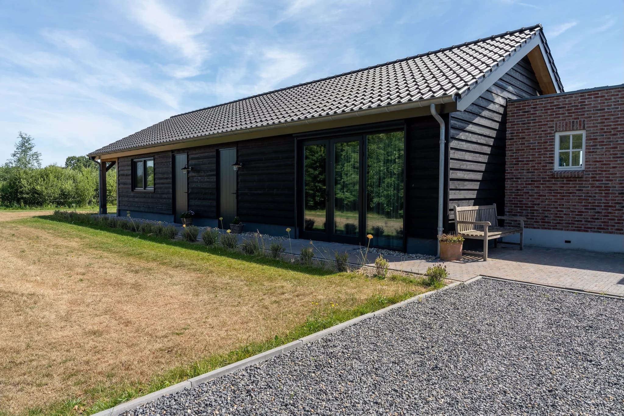 Woning met zwarte houten gevel en grijs pannendak, tuin met gras en planten, en een stenen pad