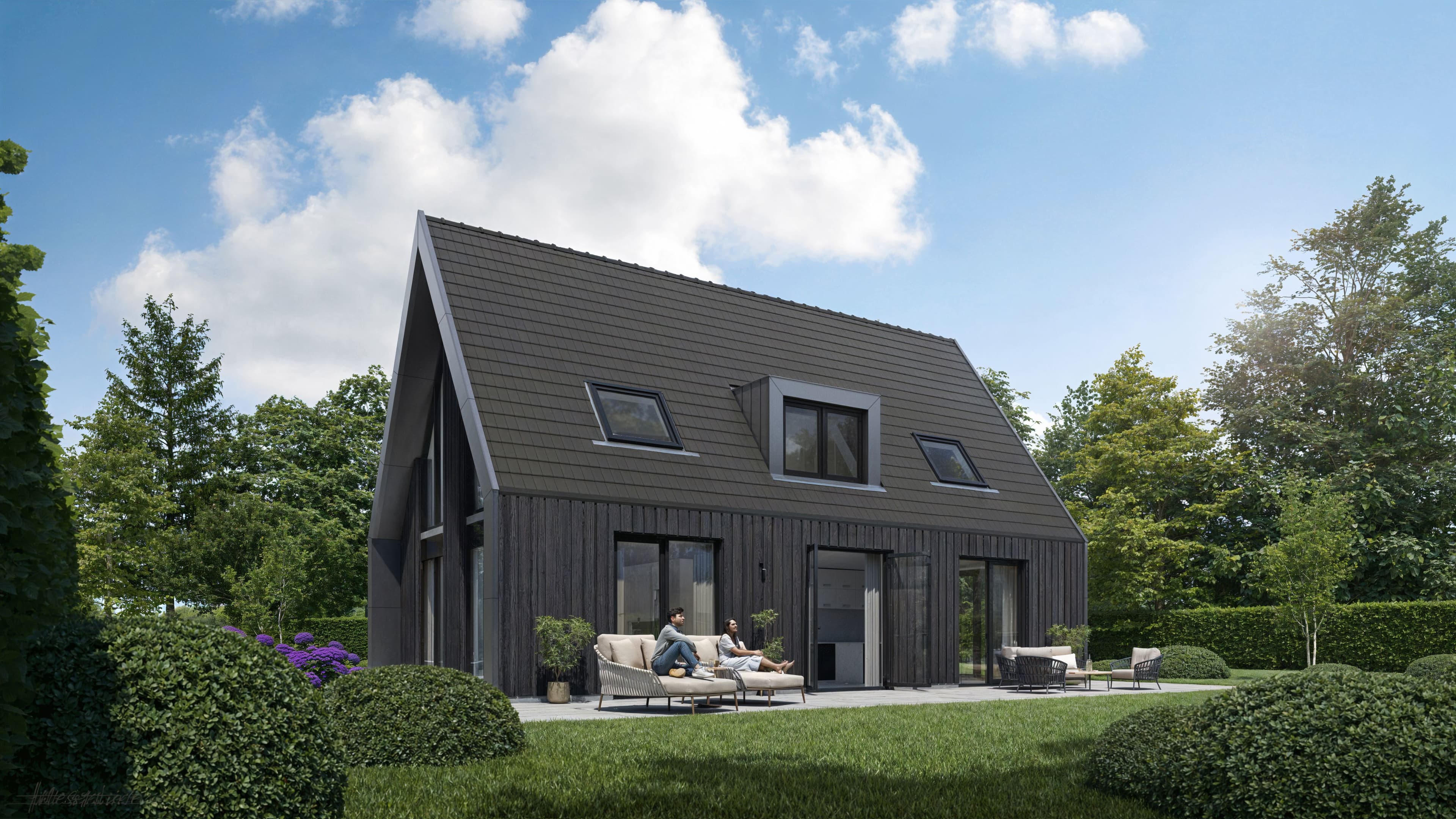 Zwarte houten woning met zadeldak en groot terras met loungemeubilair en twee mensen zittend in een groene tuin onder een blauwe lucht met wolken.