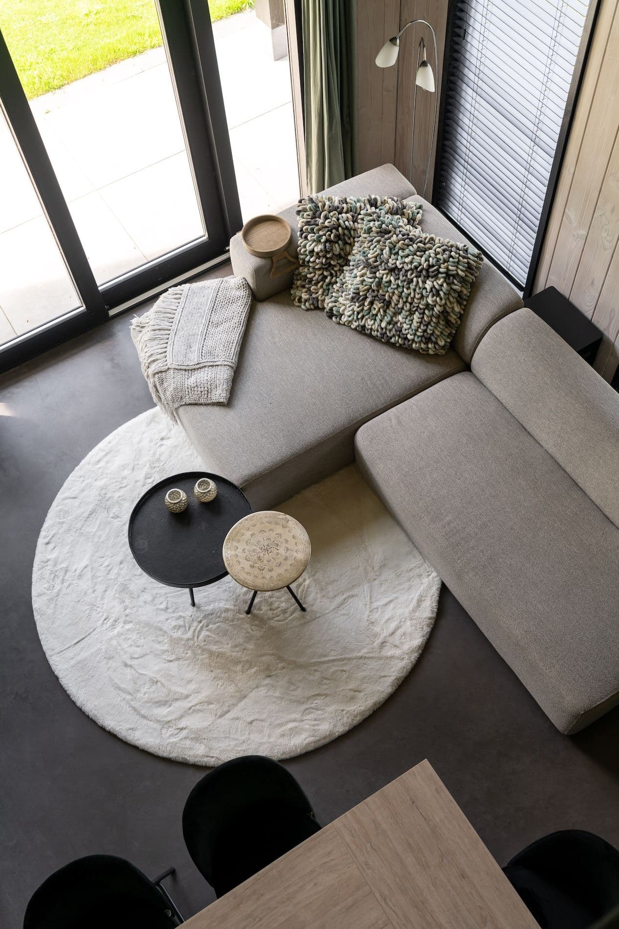 Moderne woonkamer met beige hoekbank, rond wit vloerkleed en twee kleine tafeltjes