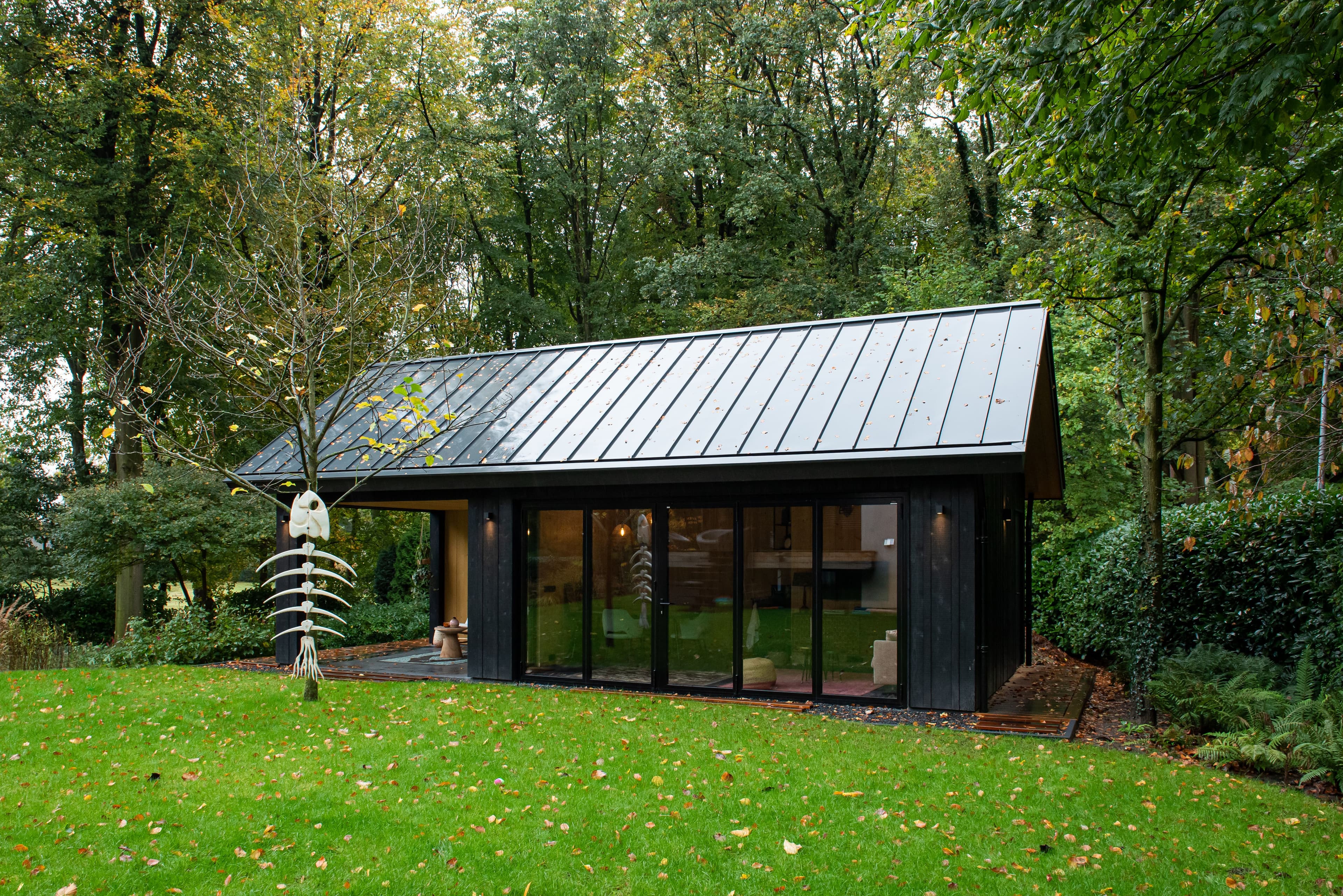 Moderne zwarte houten tuinkamer met glazen schuifdeuren en grijs metalen dak in groene tuin