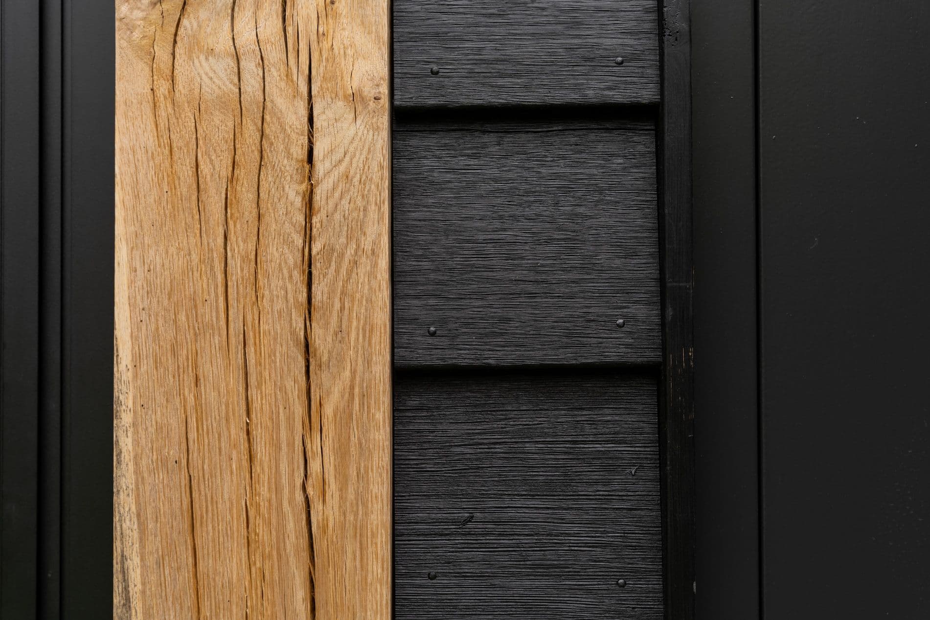 Dichtbij genomen beeld van natuurlijk houten plank naast zwart geschilderde houten planken met zichtbare schroeven.