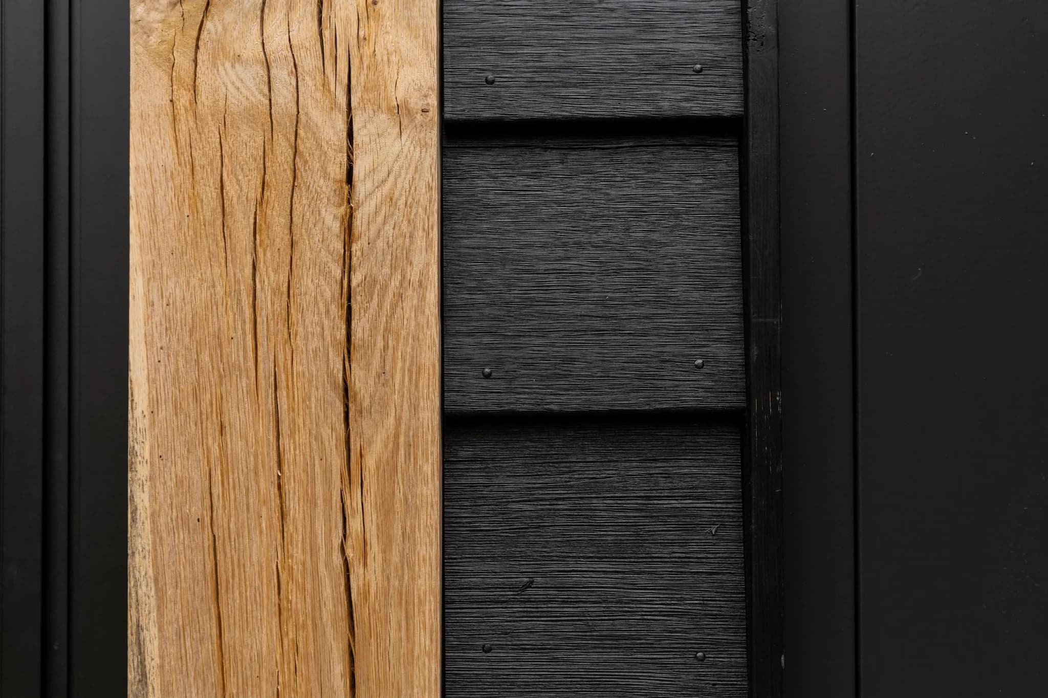 Dichtbij genomen beeld van natuurlijk houten plank naast zwart geschilderde houten planken met zichtbare schroeven.