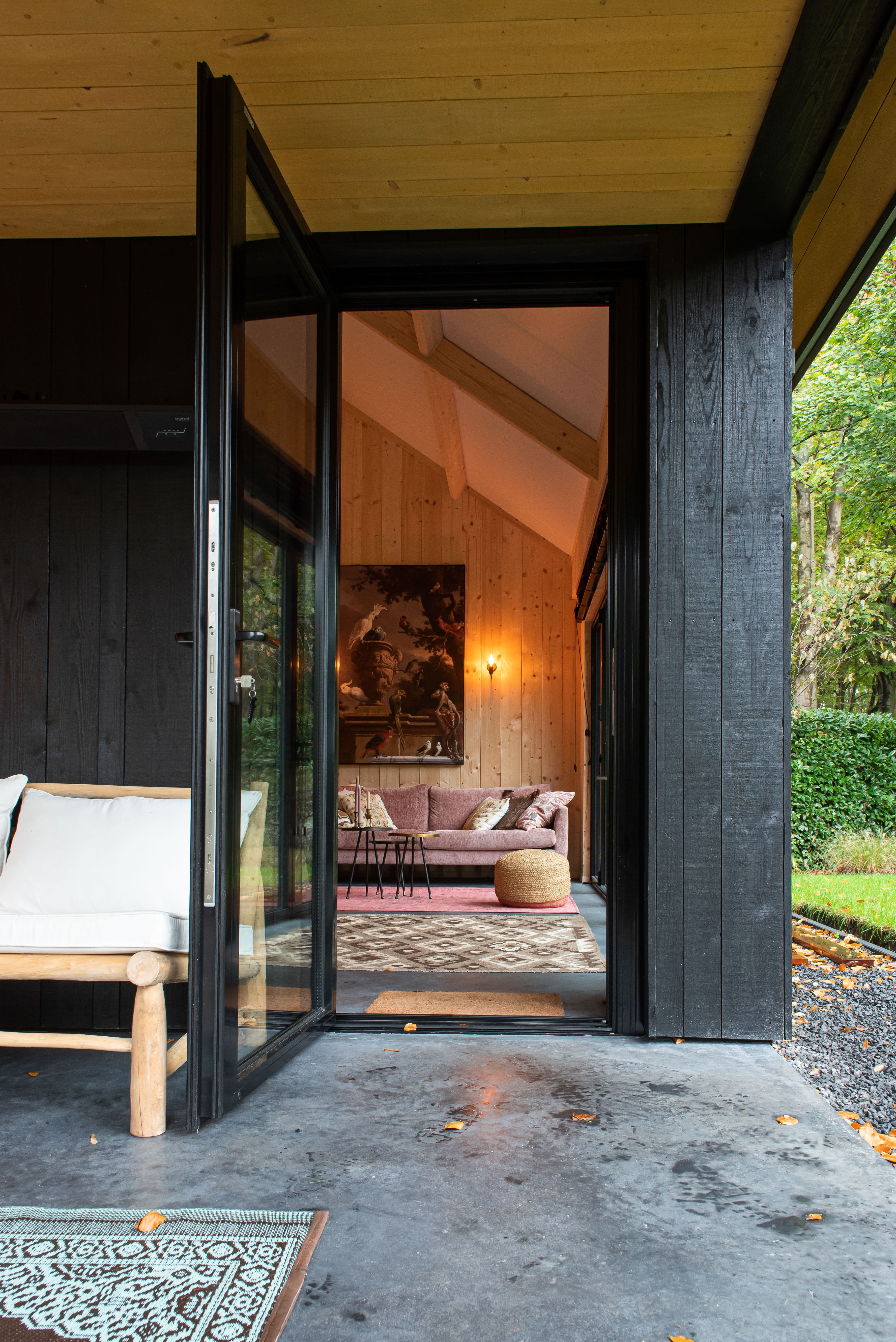 Open glazen deur van een modern houten huis met zichtbaar interieur en een roze bank