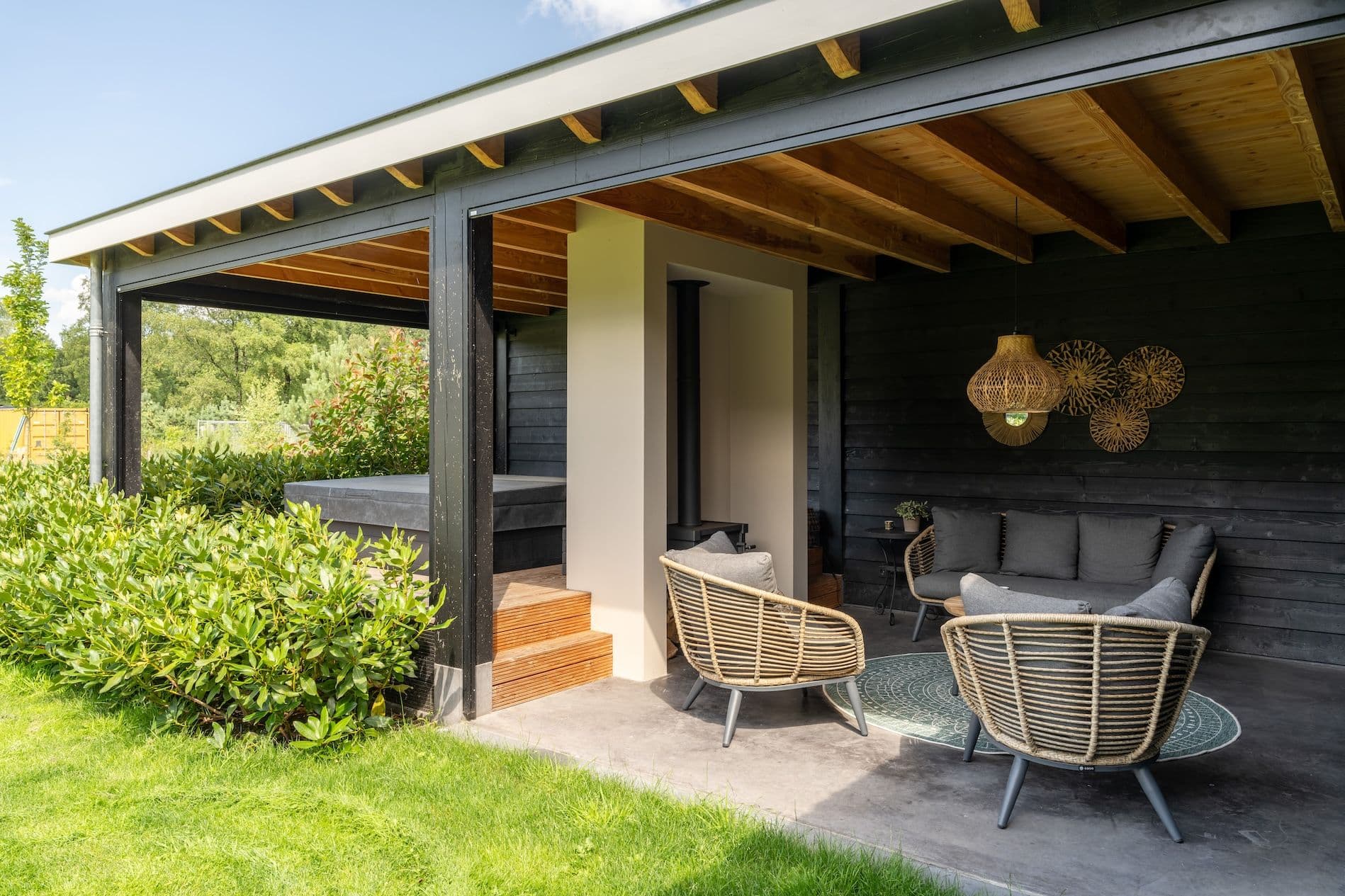 Overdekt terras met rotan stoelen en bank, haard en wanddecoratie in een groene tuin