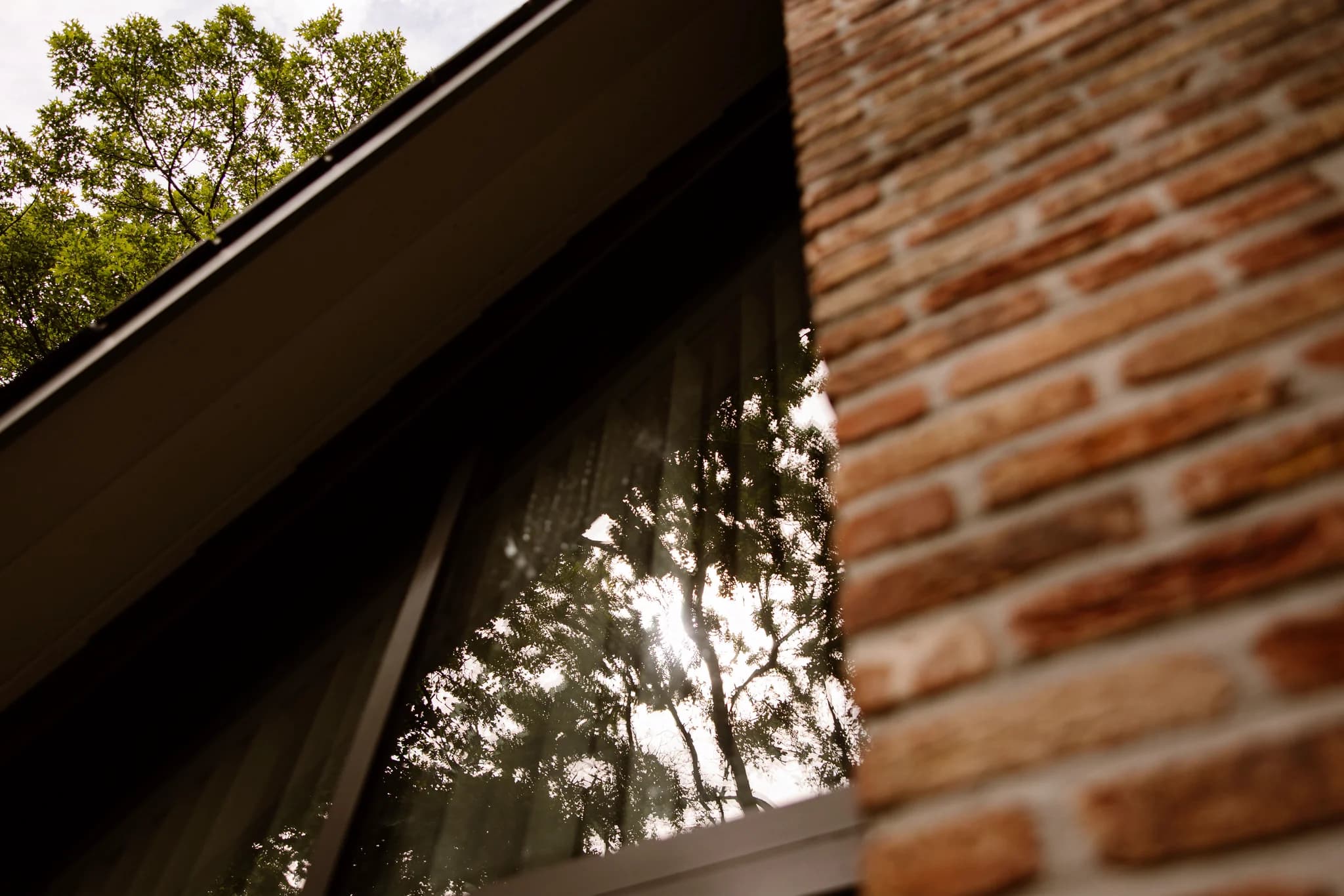 Raam weerspiegeld zon en bomen naast rode bakstenen gevel van gebouw