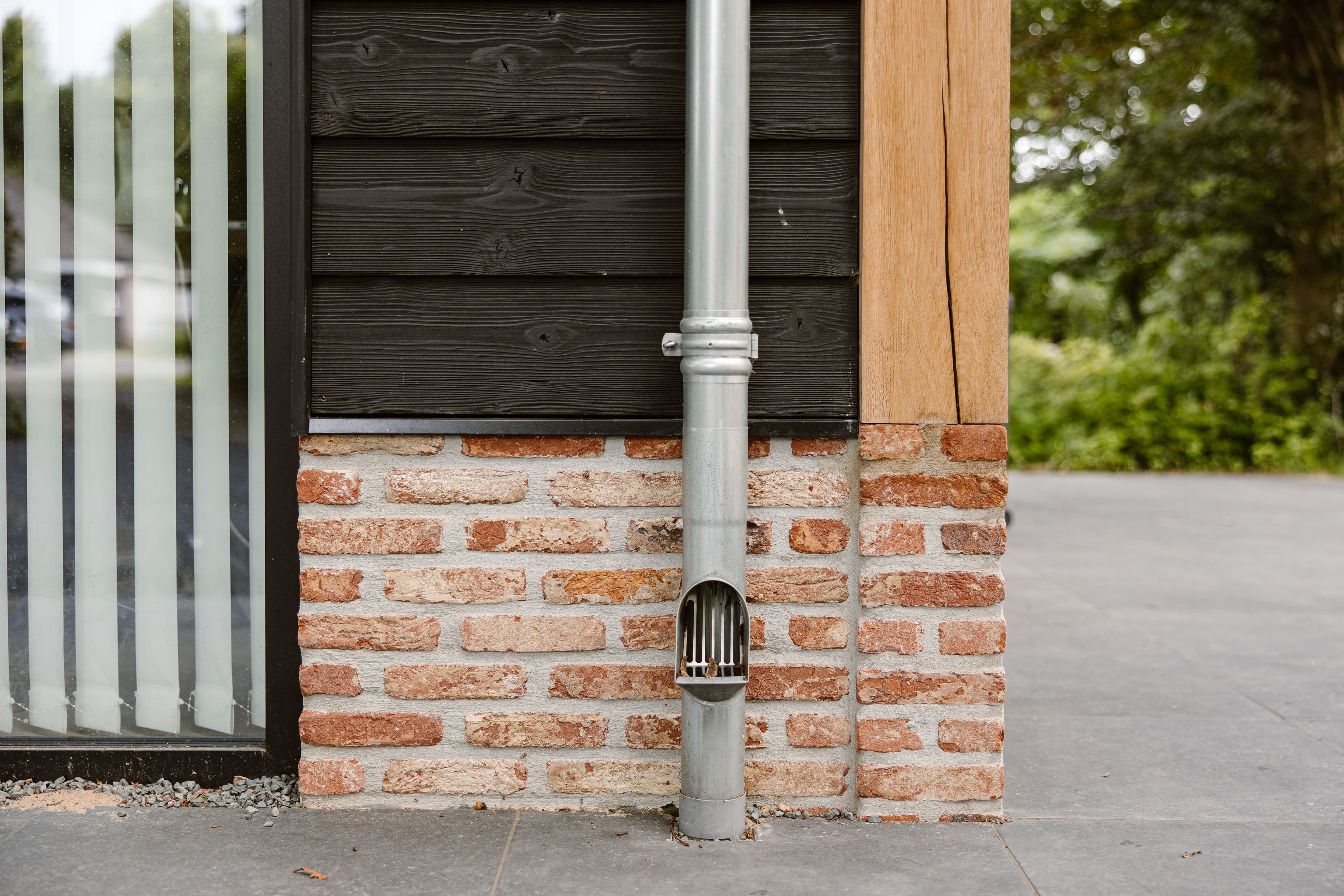 Metalen regenpijp aan gevel met bakstenen, hout en glas