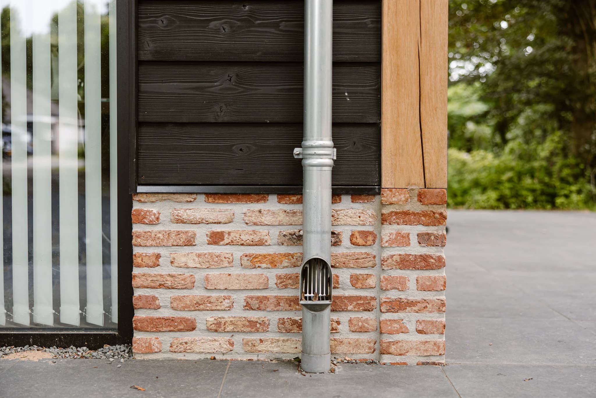 Metalen regenpijp aan gevel met bakstenen, hout en glas