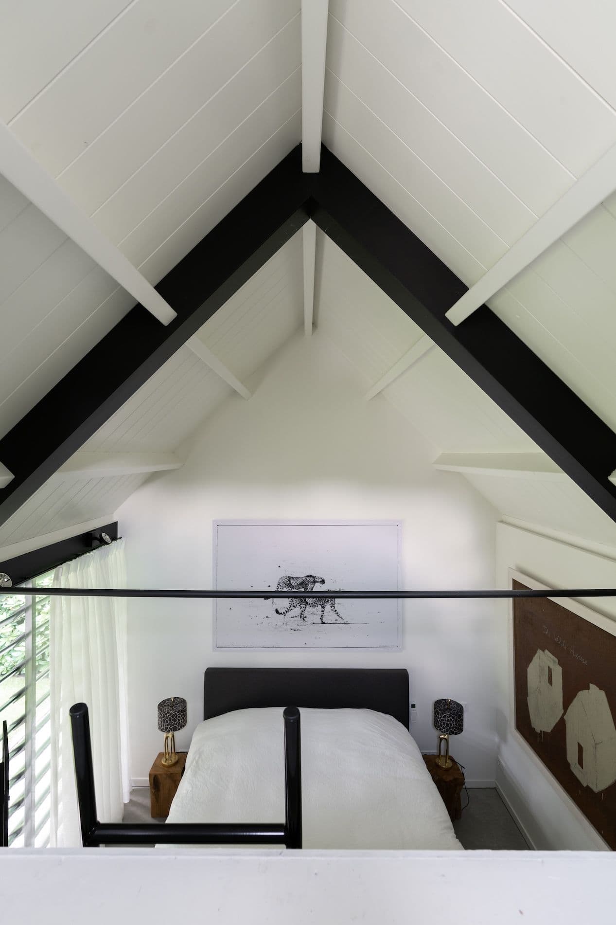 Slaapkamer met wit bed, zwarte balken aan het plafond en kunstwerken aan de muren