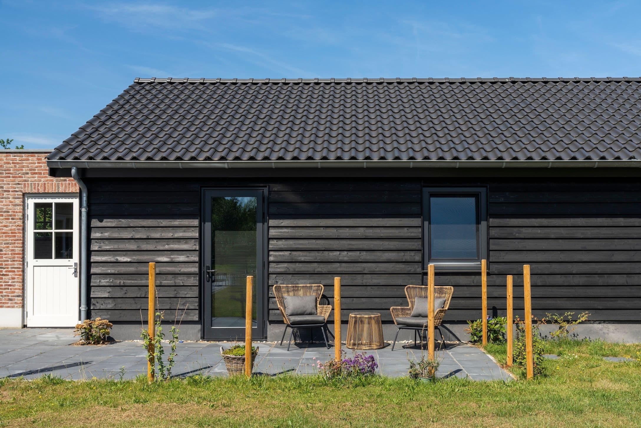 Terras met twee rotanstoelen en een bijzettafel voor een zwart houten huis.