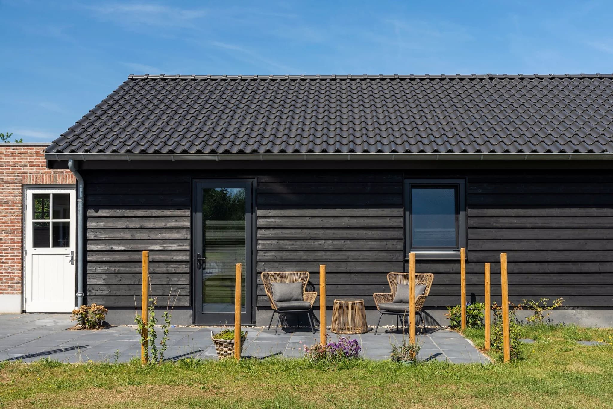 Terras met twee rotanstoelen en een bijzettafel voor een zwart houten huis.