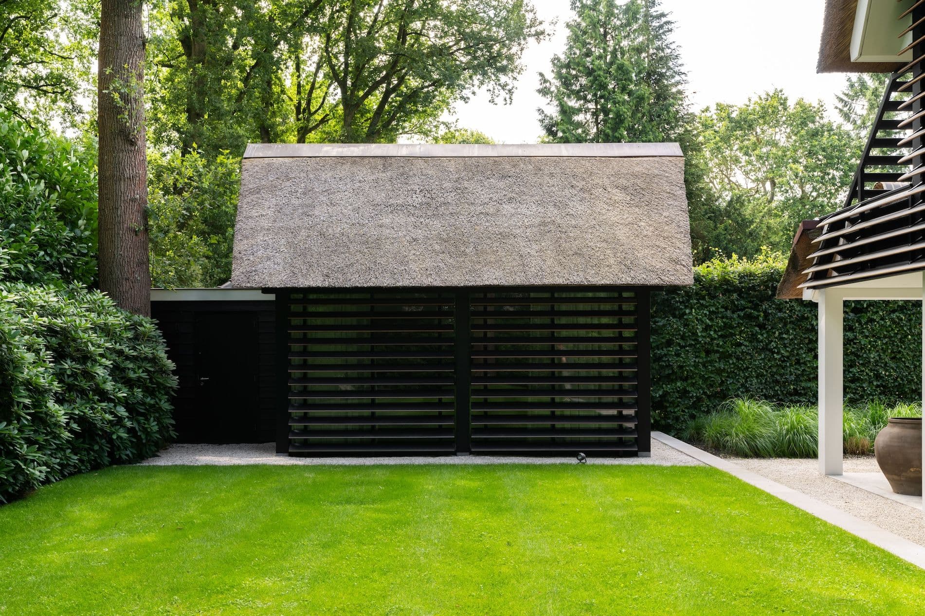 Tuin met groen grasveld en twee gebouwen met rieten daken en zwarte lamellen