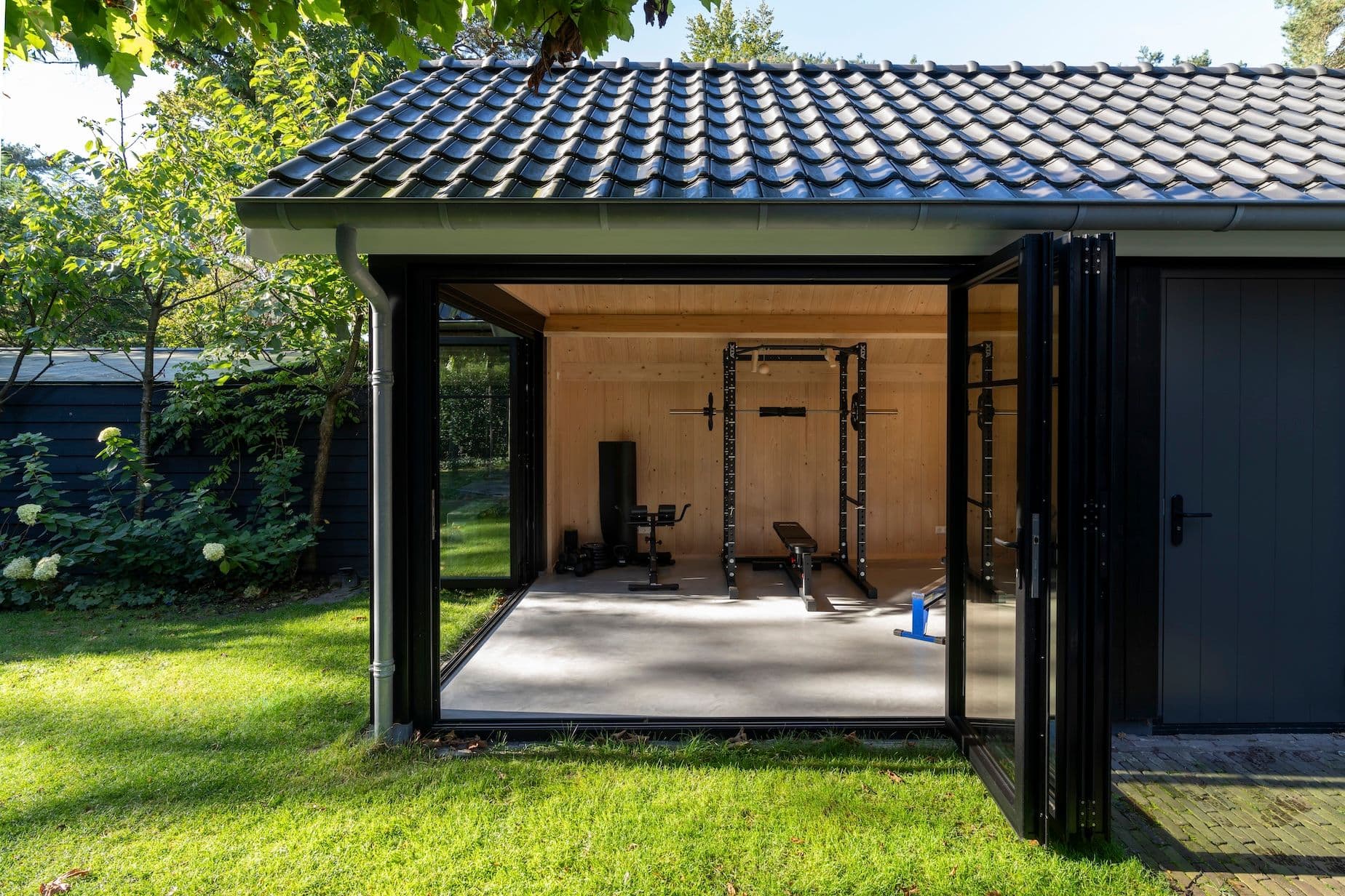 Tuinberging met open zwarte vouwwand en binnenin fitnessapparatuur zoals halterrek en bankje