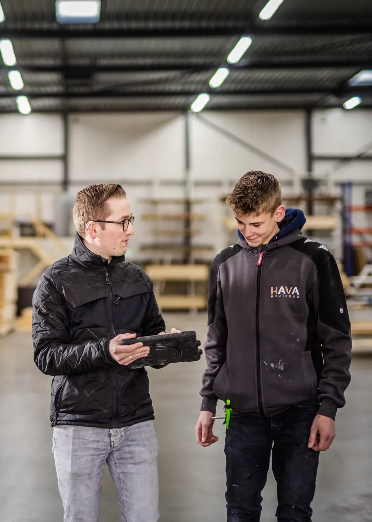 Twee mannen in een werkplaats, een toont een zwart object aan de ander.