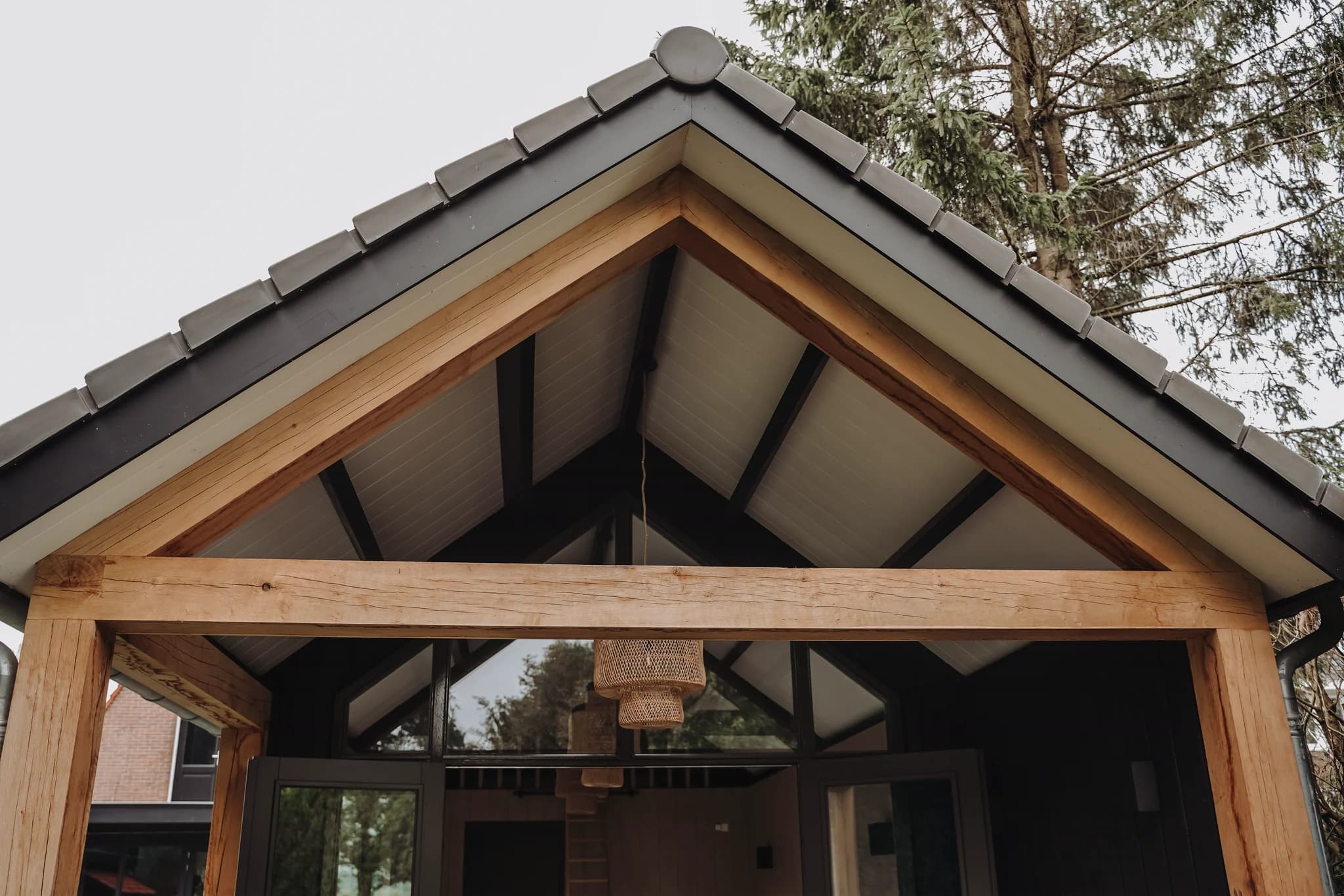 Voorgevel van een modern houten huis met een zadeldak en een houten overkapping met glas