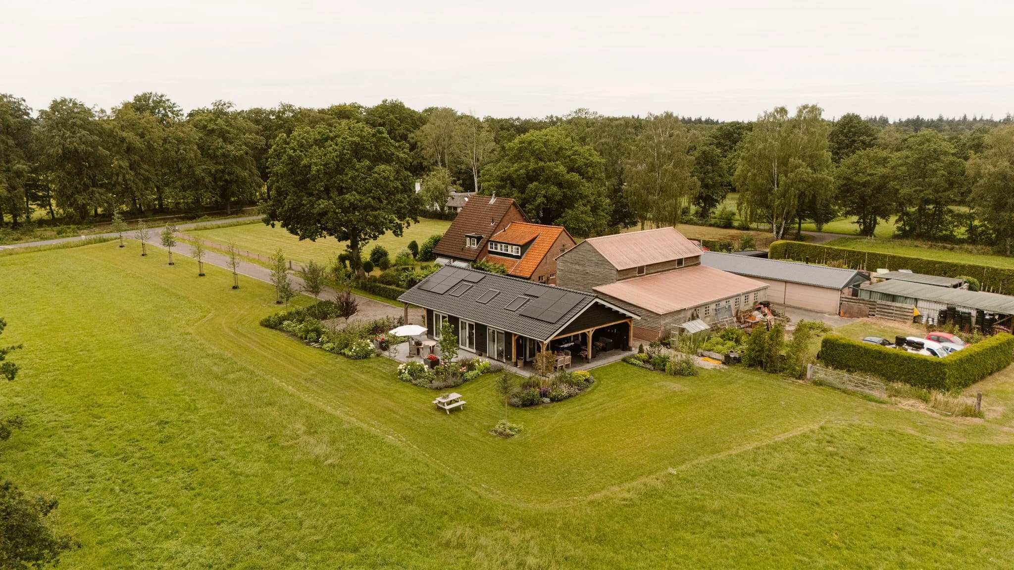 Woonboerderij met grote groene tuin en schuren in een landelijke omgeving gezien vanuit de lucht