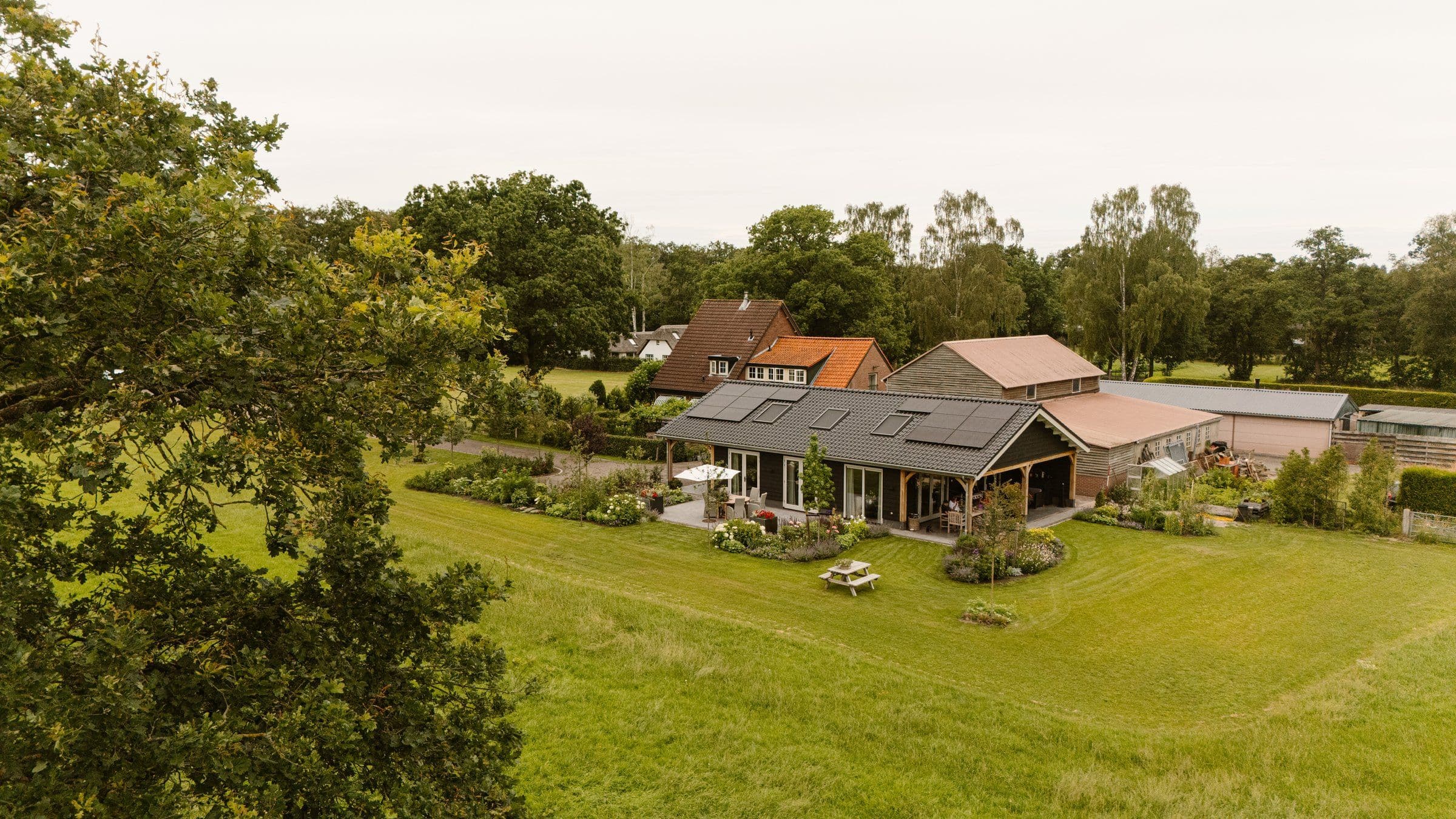 Luchtfoto van een huis met zonnepanelen op het dak en een groene tuin met gras en bomen