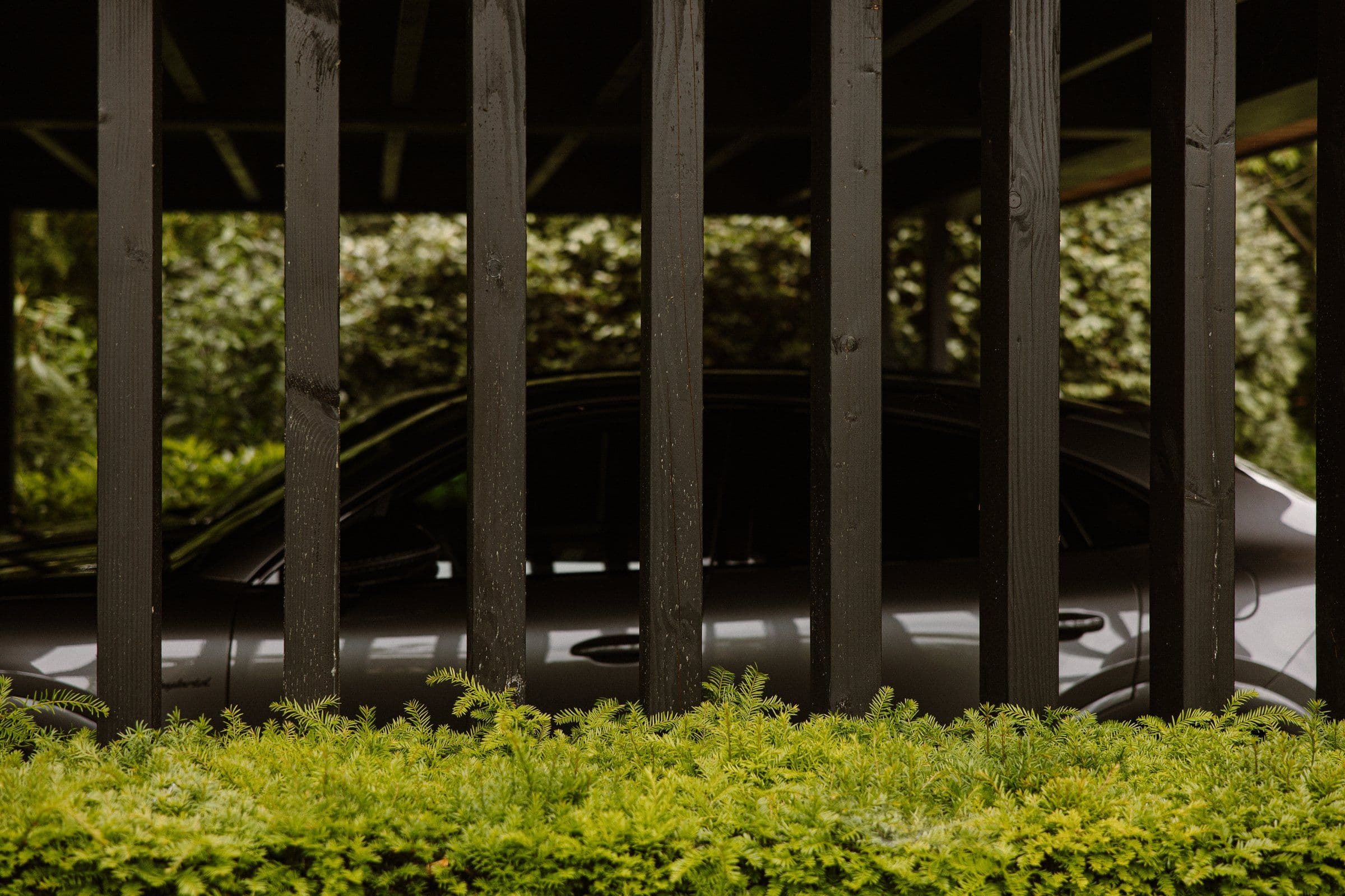 Grijze auto zichtbaar door verticale houten houten planken met groene struiken op de voorgrond