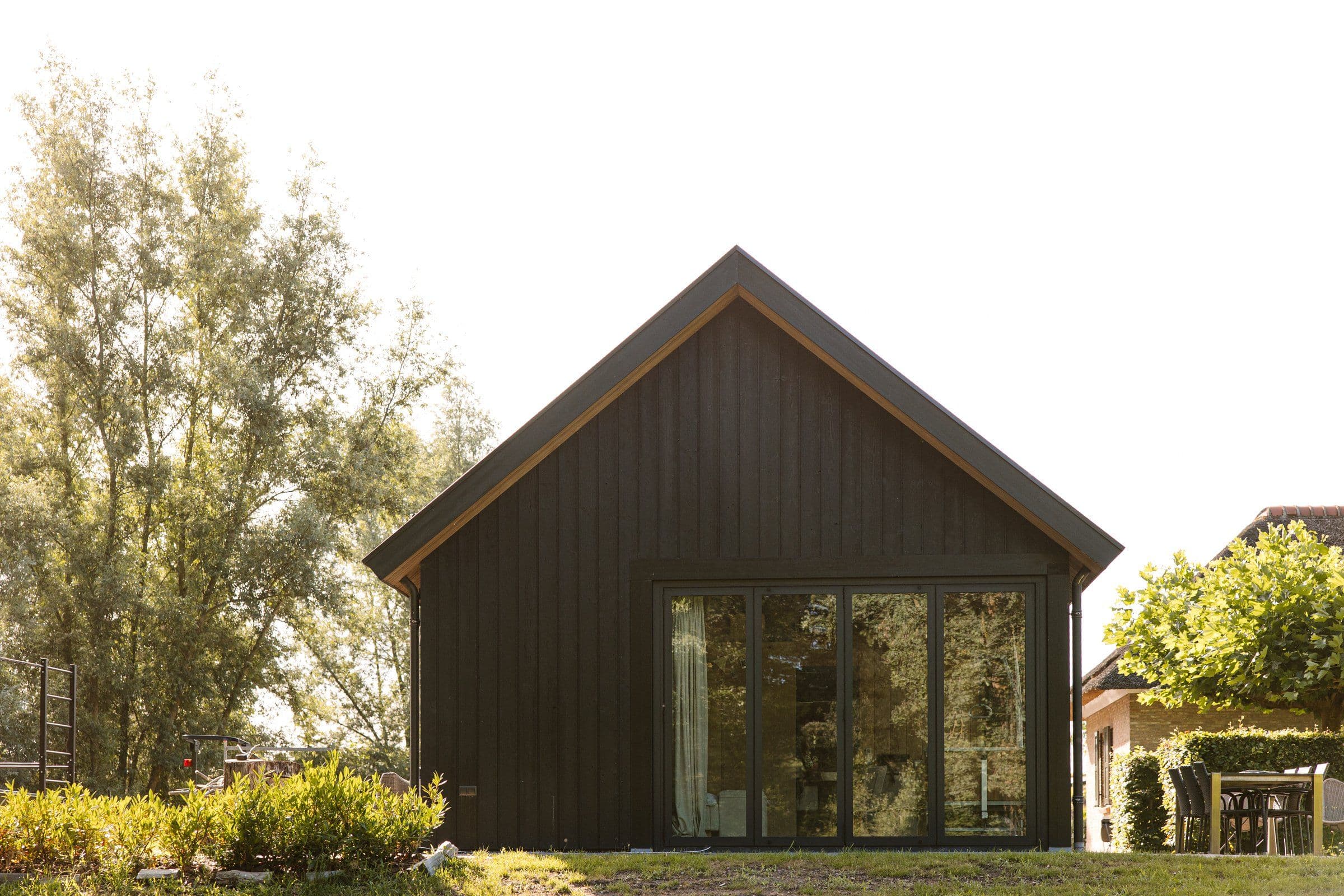Achterkant van een zwart houten huis met grote glazen schuifdeuren en groen rondom.